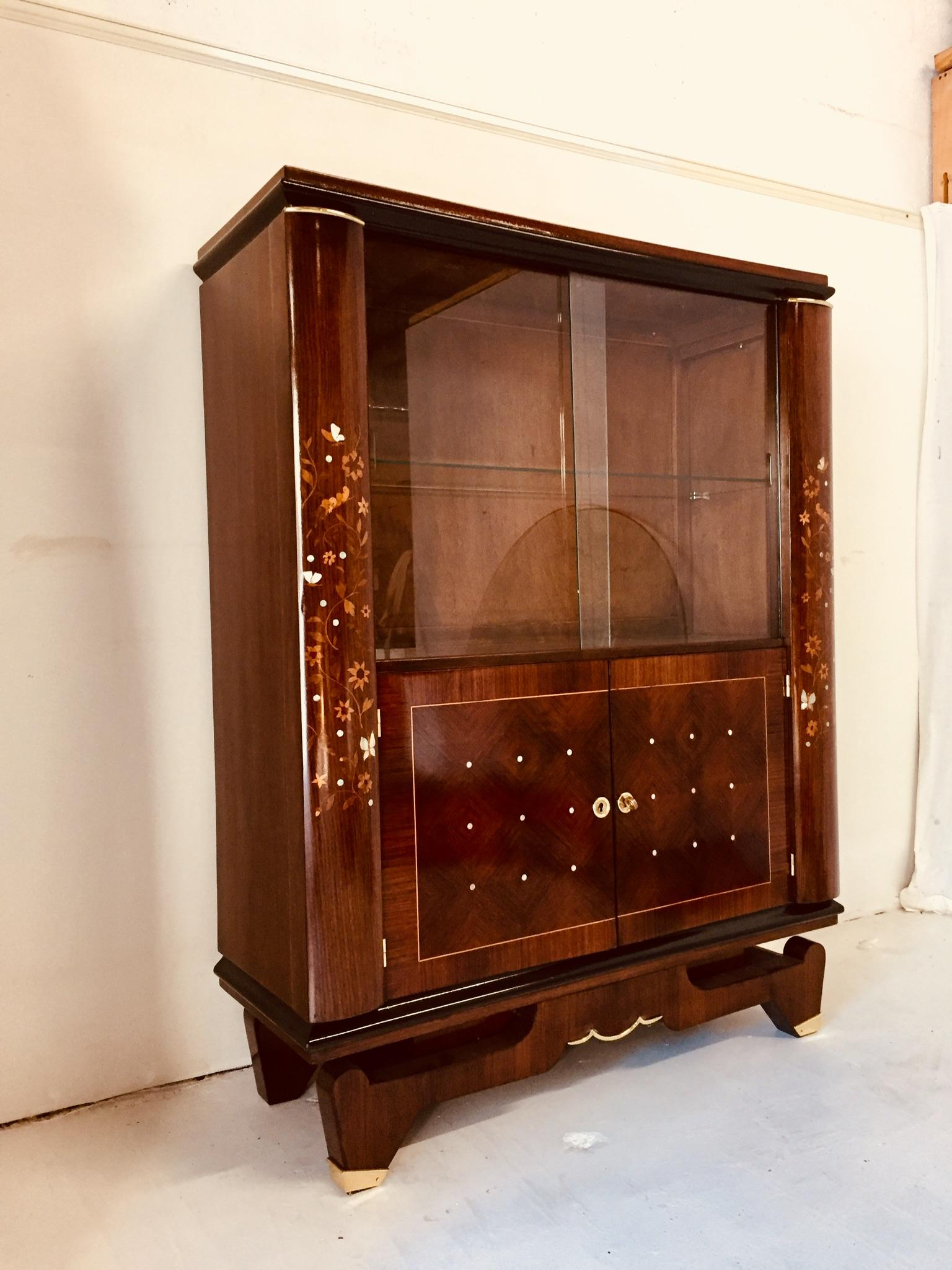 Great quality craftsmanship for the display cabinet in the style of Jules Leleu.
Late Art Deco period.
One glass shelf in the upper part of the furniture.
Two doors on the basement.
Bronze accents on the top of each column and on the feet.
  