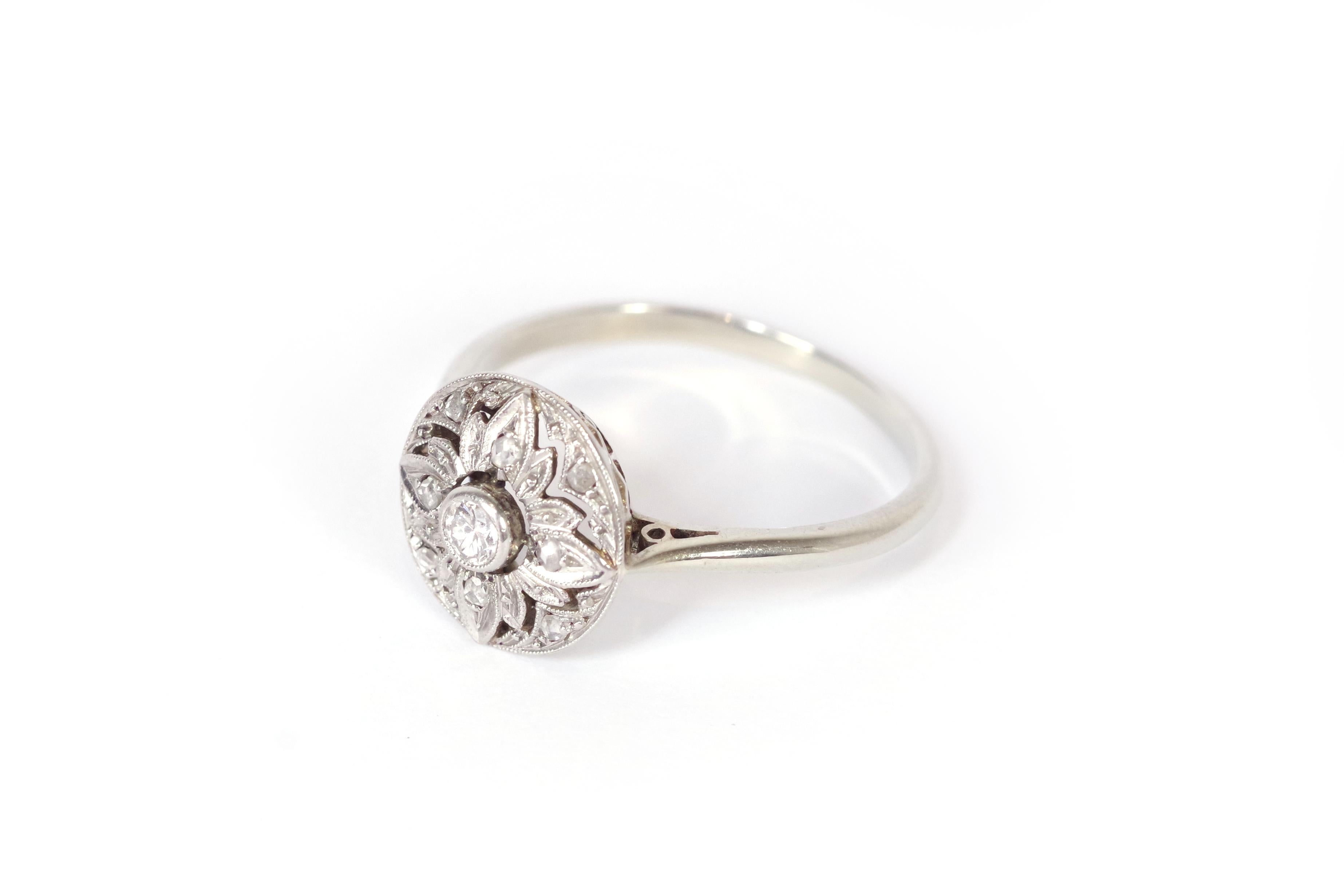 Art Deco round diamond ring in 18 Karat white gold and platinum. This Art Deco ring features a circular centerpiece with a brilliant-cut diamond in a beaded setting. The ring showcases geometric lines in beaded white gold forming a stylized flower