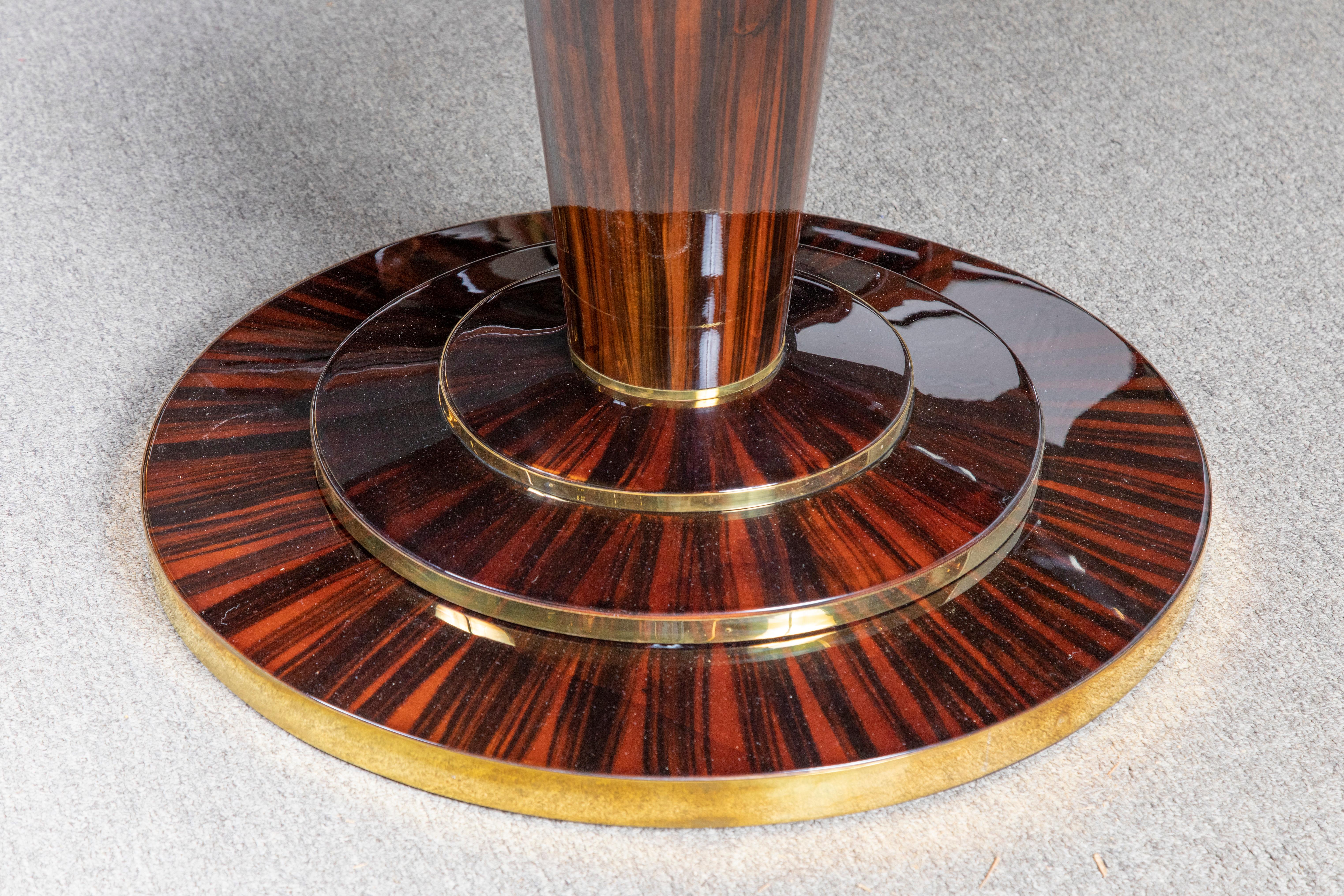 Round table top displays beauty of the high quality Macassar wood. It is supported by the slim leg that is attached to the round base. The top of the base has brass decorative elements wrapped around it. 
Re-polished. Condition is