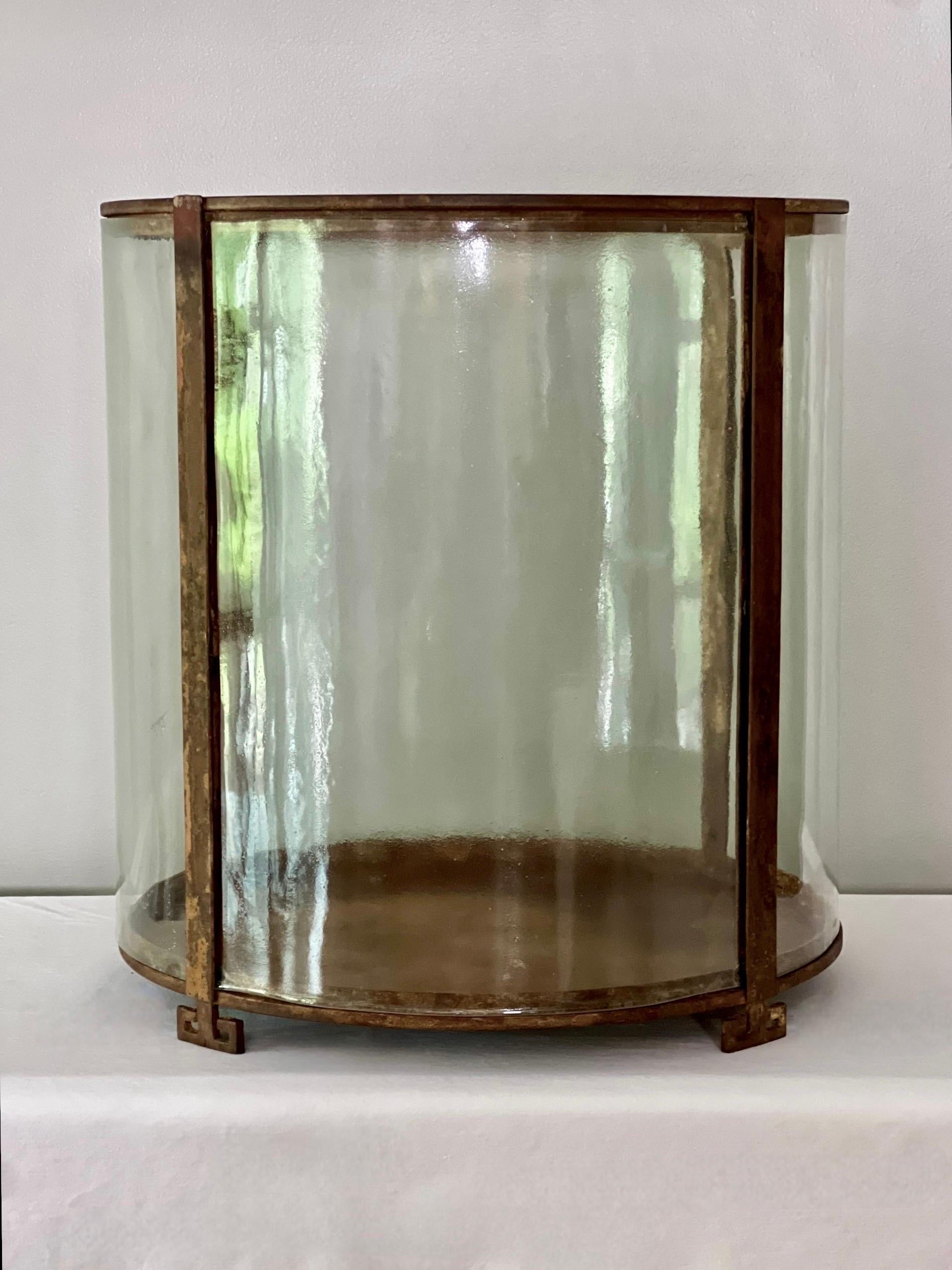 Large Art Deco period round iron and glass open-air terrarium or display showcase, circa 1910s.  A unique vitrine with four original curved glass panels secured within an iron frame raised on Greek key feet.  A stunning statement piece for a large