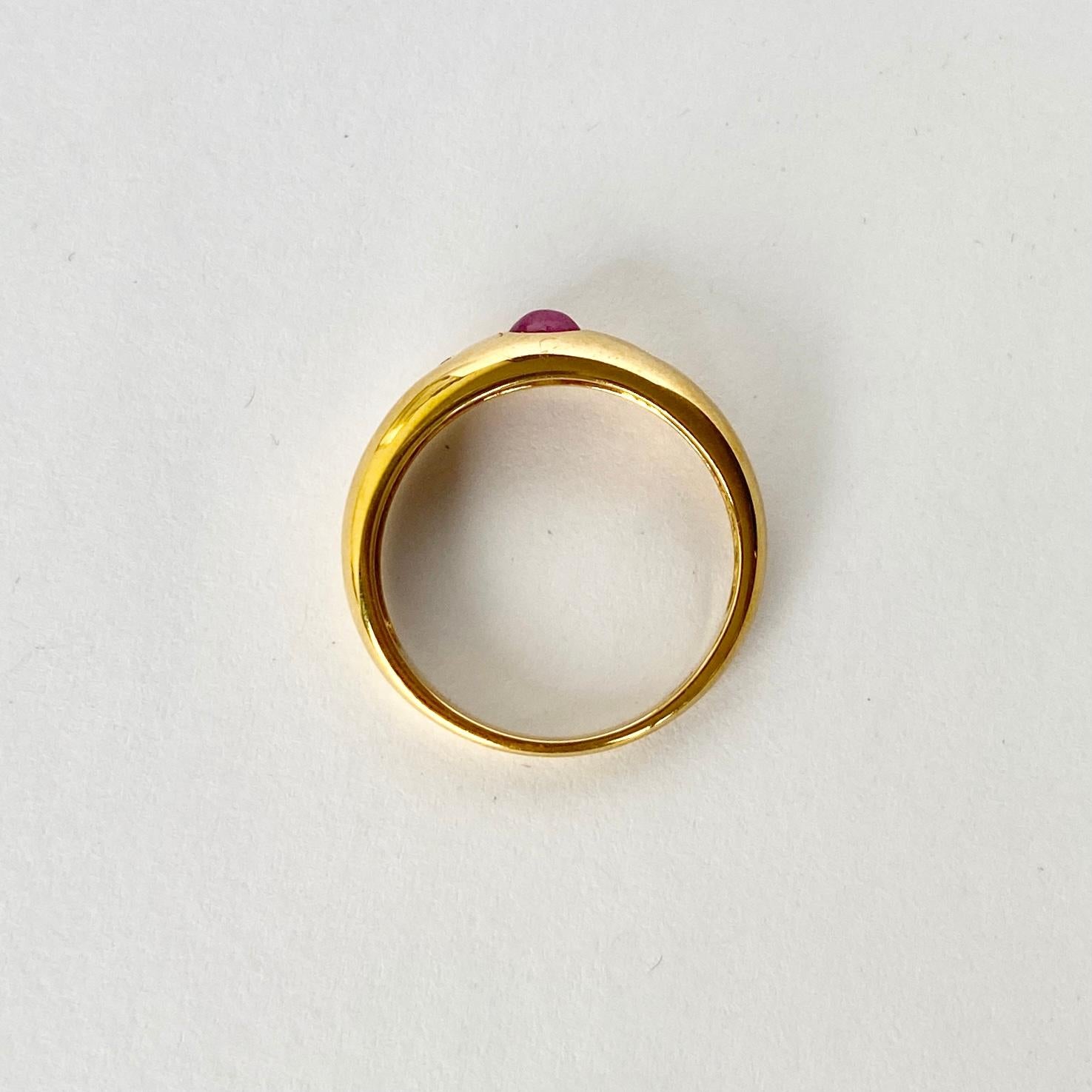 Dieses wunderschöne Band aus 18 Karat Gold trägt einen Rubin-Cabochon mit funkelnden Diamanten an beiden Seiten. Diamant insgesamt 8 Punkte.

Ring Größe: L 1/2 oder 6 
Breite des Bandes: 5,5 mm

Gewicht: 2,75 g