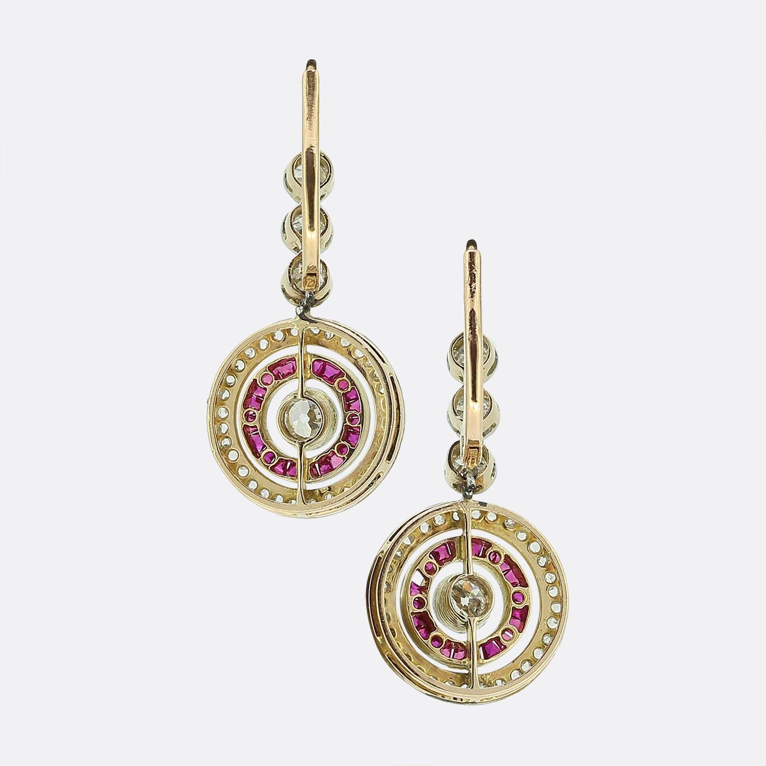 Ecco uno splendido paio di orecchini a goccia realizzati in un'epoca in cui lo stile Art Déco era all'apice del design. Ogni pezzo presenta un trio di diamanti rotondi sfaccettati di taglio antico che sospende un motivo a bersaglio composto da una