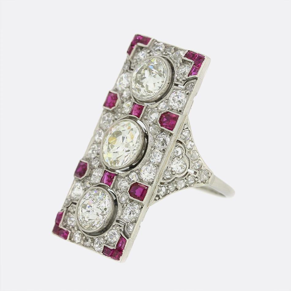 This is a platinum Art Deco ruby and diamond tablet ring. The ring has been set with three large old cut diamonds within a rose cut diamond setting crafted in platinum. Additionally, the ring has been set with multiple mixed calibre cut rubies and