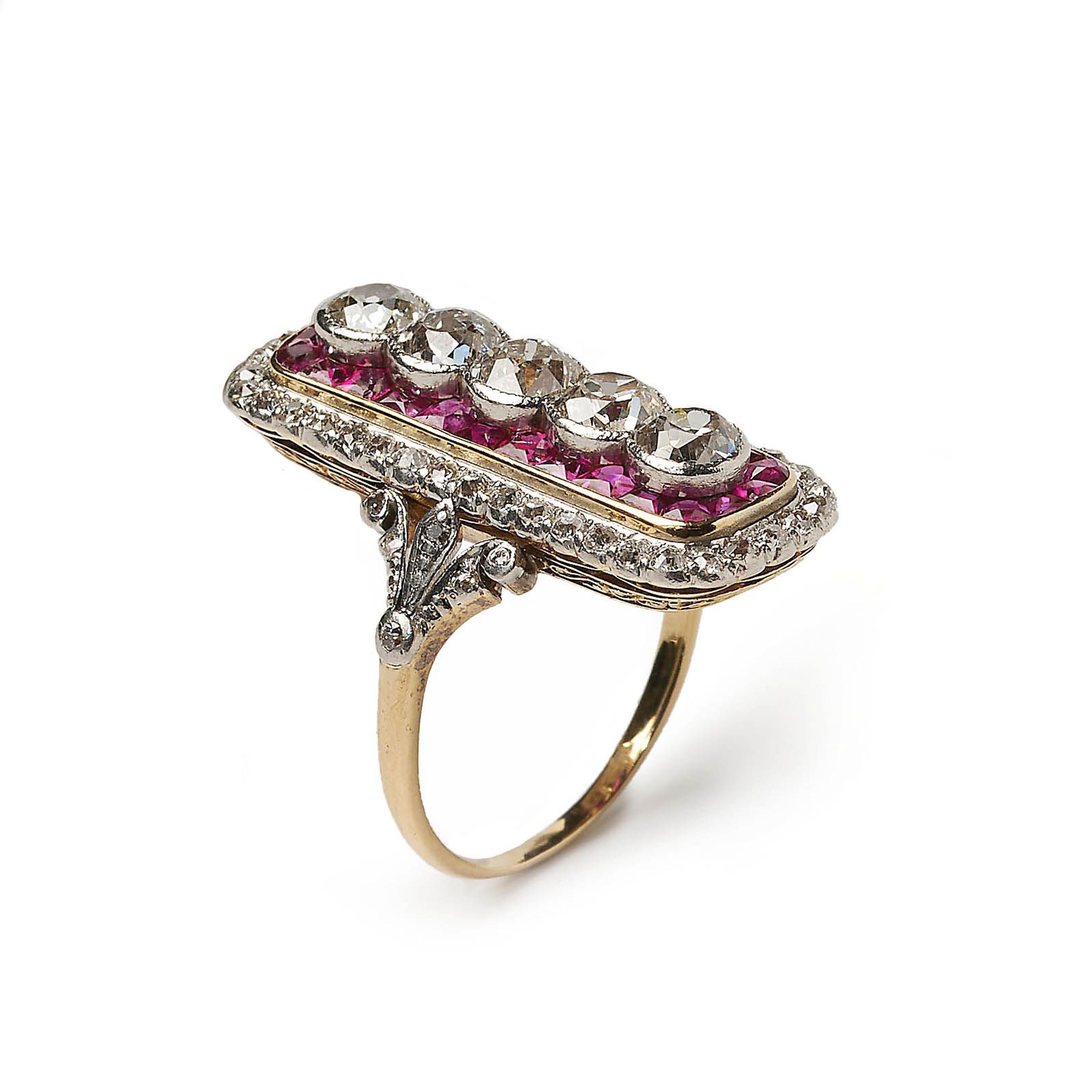A ruby and diamond early Art Deco plaque ring, with five principle old-cut diamonds, set horizontally, in platinum rub over settings, with a surround of calibré rubies, in a rectangular, gold, rub over setting, with rounded corners, with a border of