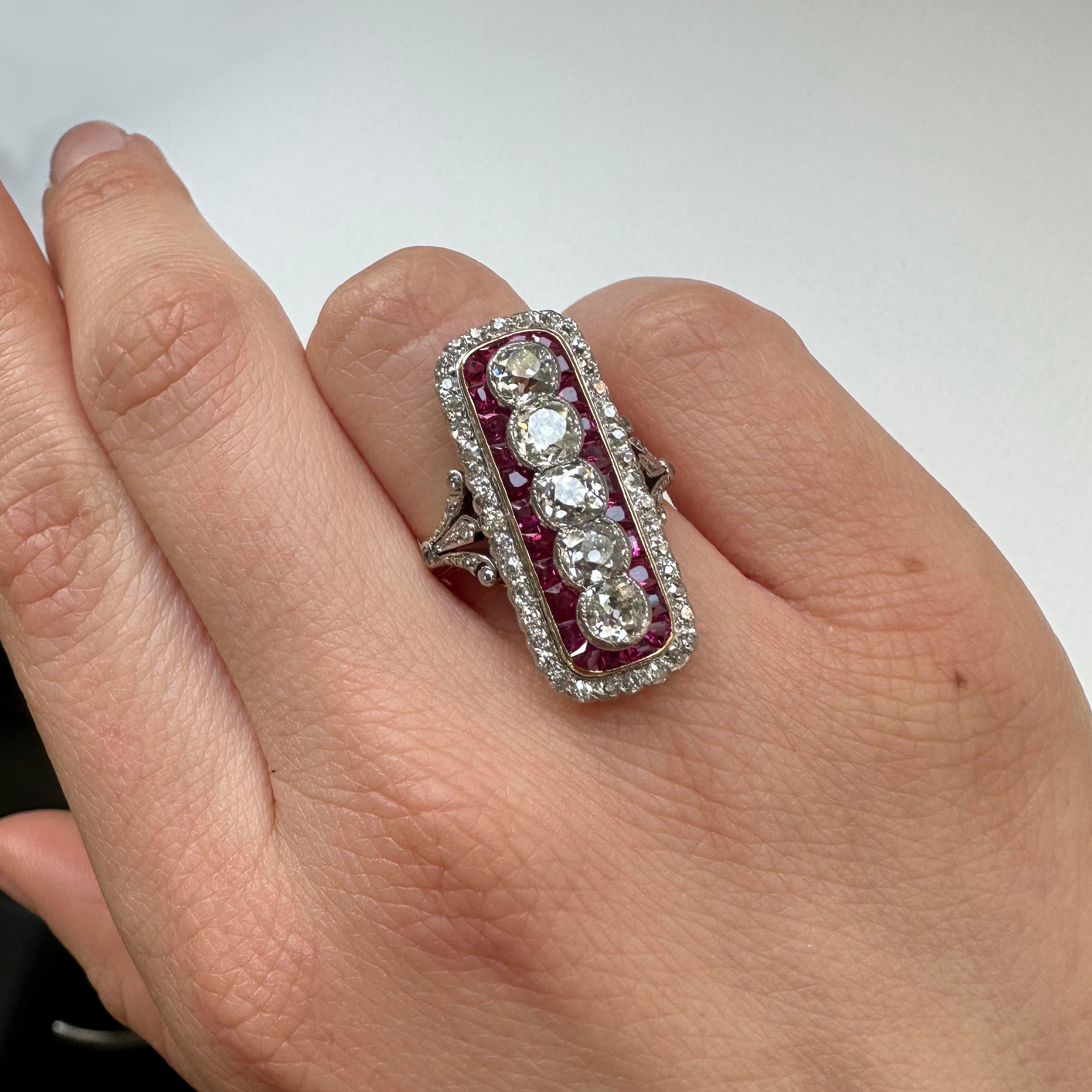 A ruby and diamond early Art Deco plaque ring, with five principle old-cut diamonds, set horizontally, in platinum rub over settings, with a surround of calibré rubies, in a rectangular, gold, rub over setting, with rounded corners, with a border of