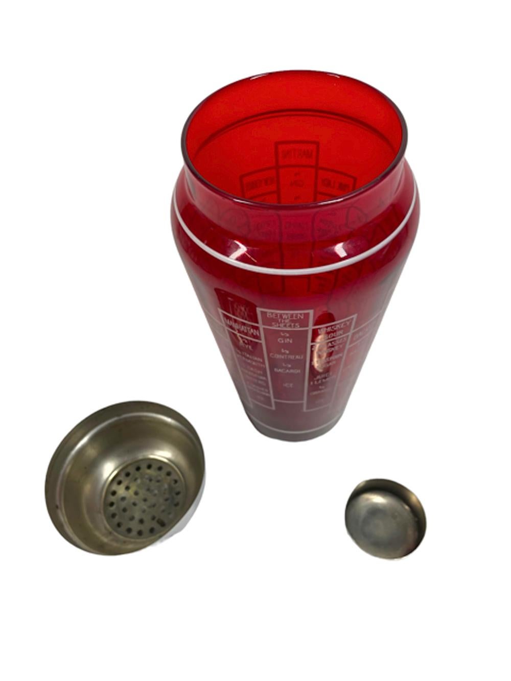 Art Deco ruby glass cocktail shaker of tapered shouldered form with 2-part chrome domed lid with integral strainer. The exterior of the shaker with white graphics having vertical stacks of blocks with recipes for 16 cocktails.