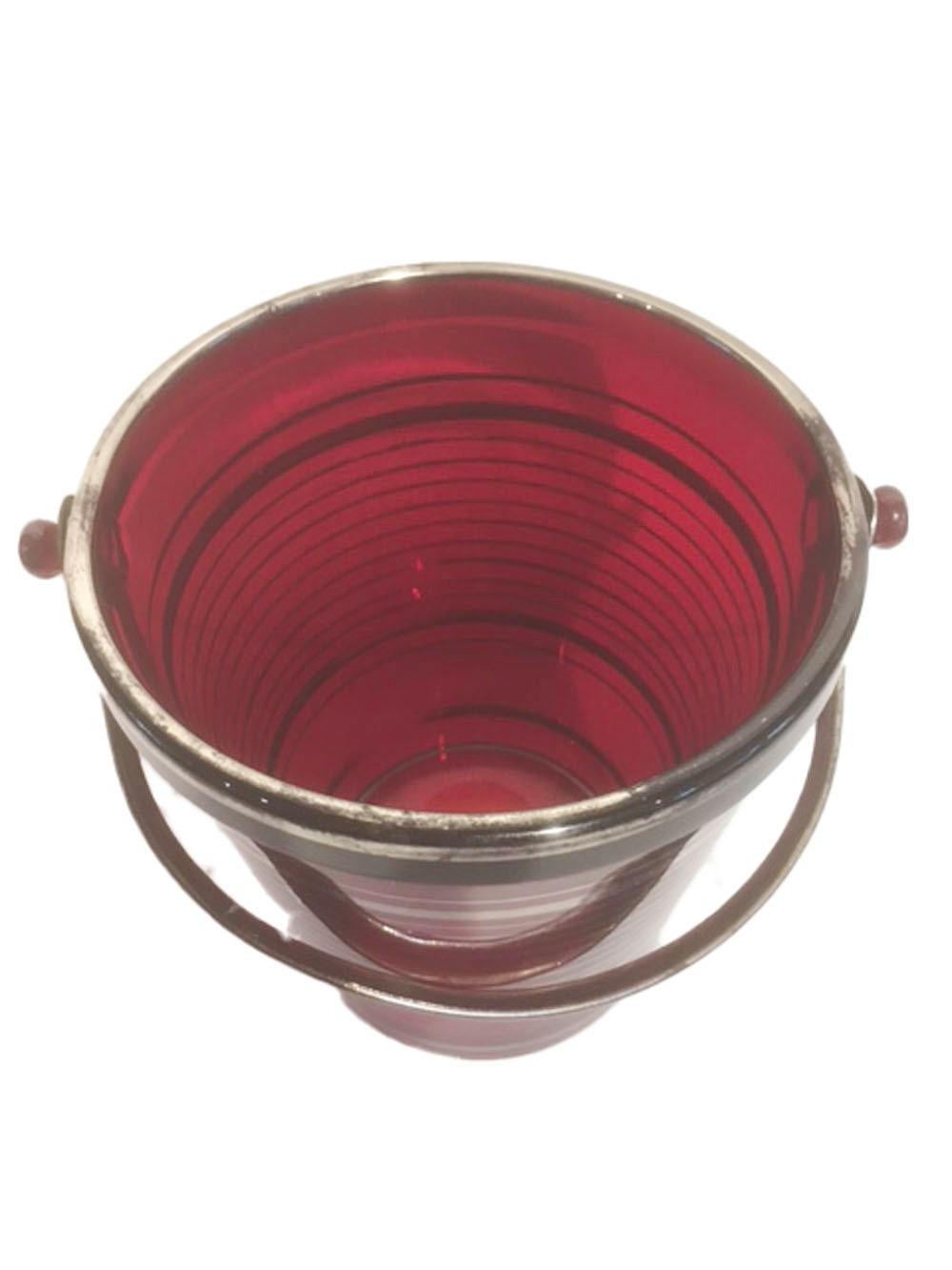 Art Deco deep red glass ice bucket with applied silver bands. The tapering pail form bucket has a raised rim with molded glass lugs where the metal handle attaches.