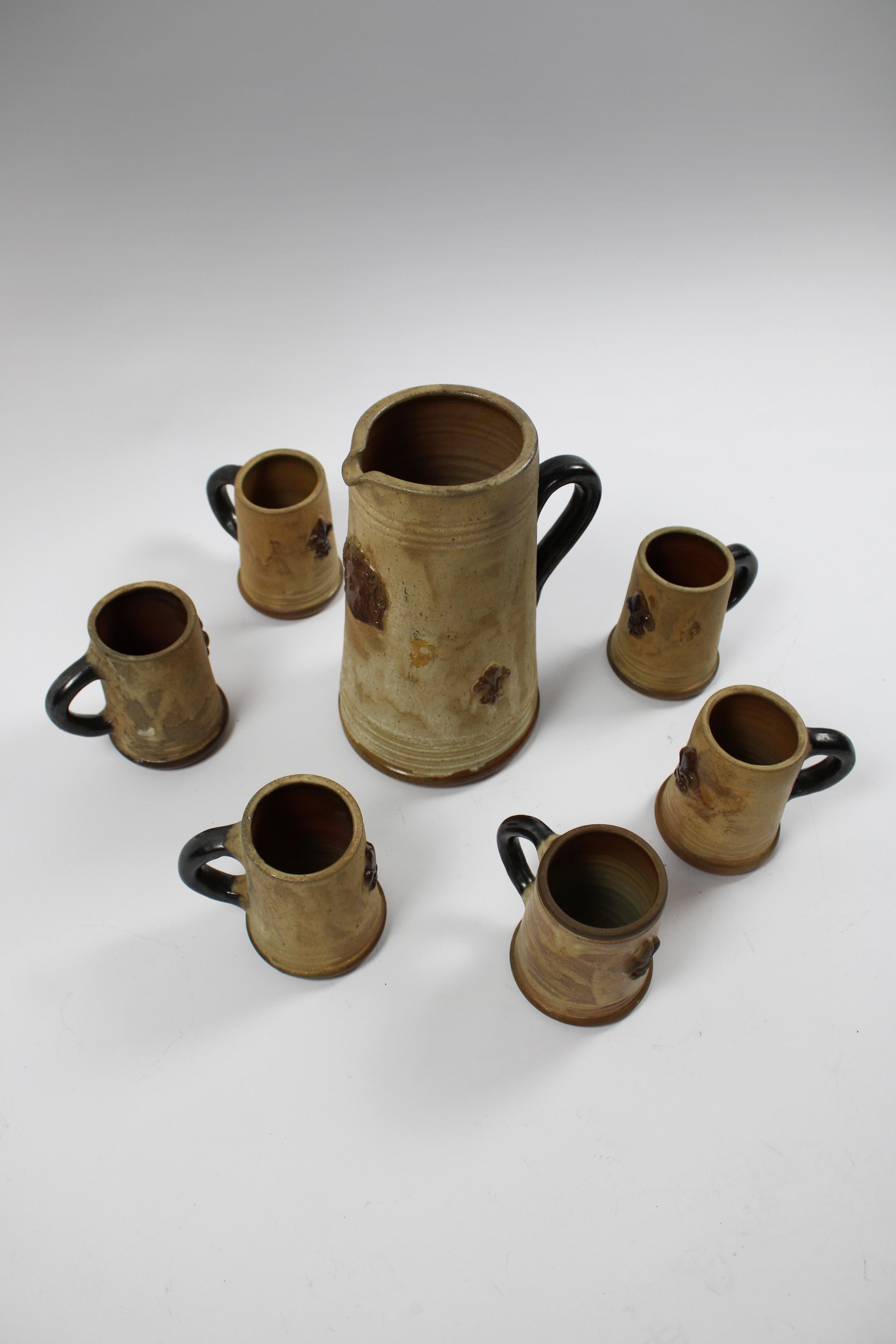 Voici un superbe ensemble Art déco comprenant un pichet en grès émaillé au sel et six chopes assorties, signés par le célèbre céramiste.
Roger Guerin de Belgique. Cet ensemble exquis est orné d'un magnifique motif Fleur de Lys, symbole d'élégance et