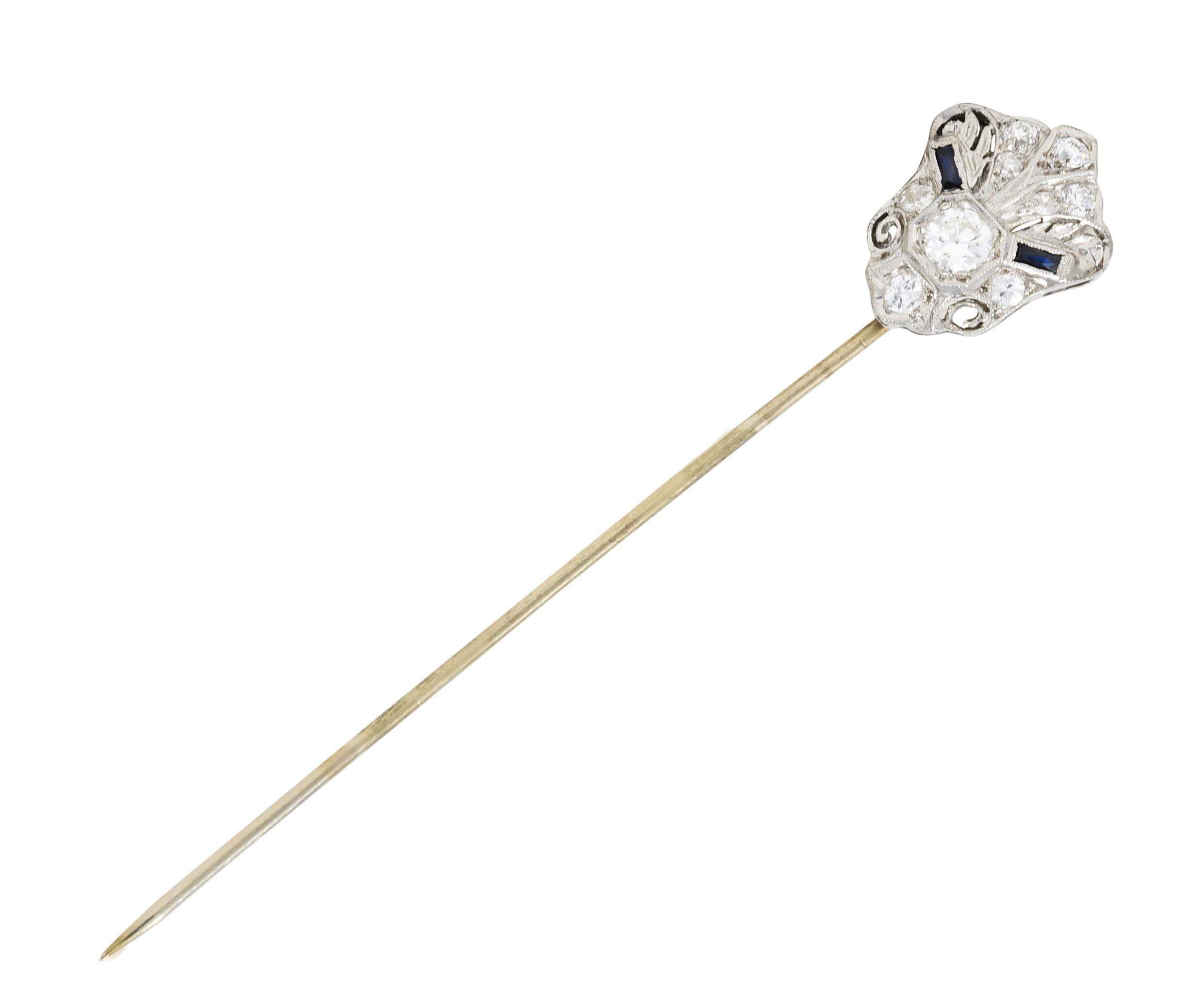 Cartouche style stickpin is accented by scrolled volutes and synthetic sapphire

While centering an old European cut diamond weighing approximately 0.27 carat - I/J color and SI1 clarity

With old European cut and single cut diamonds weighing in