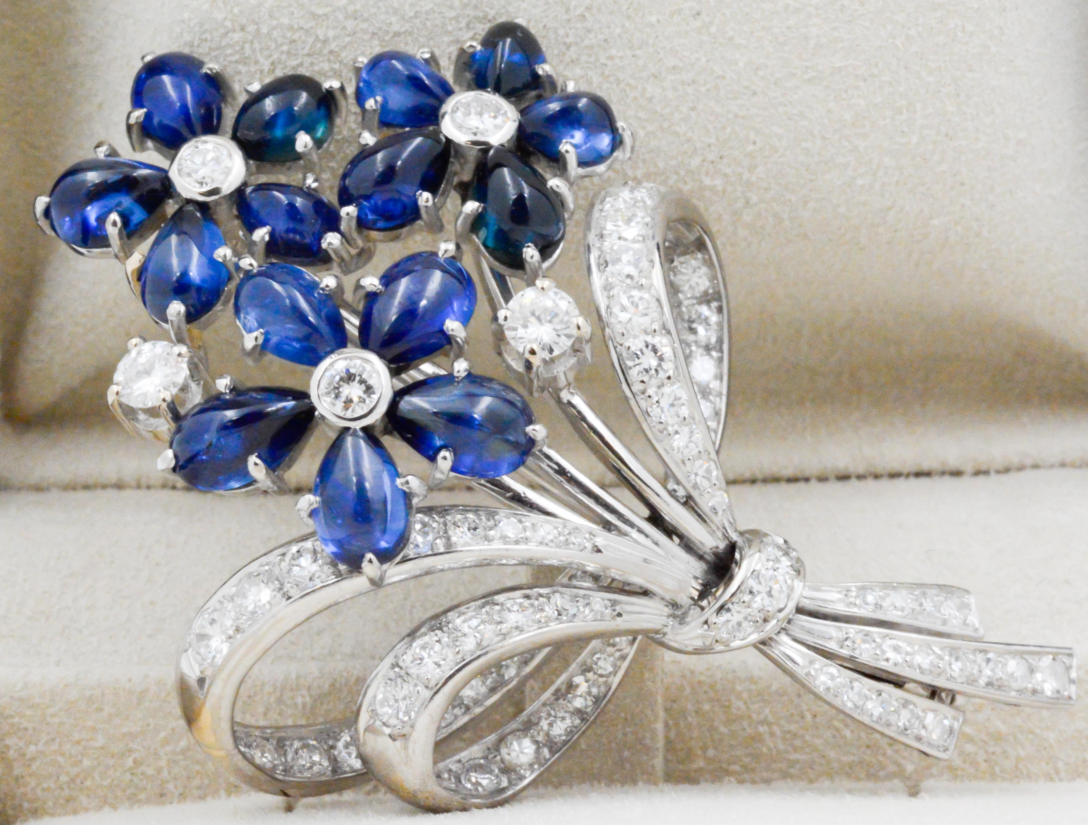This Art Deco/Retro brooch showpieces deep blue sapphires in 3 flowers all tied up with a diamond bow. This creative brooch is crafted in 18 karat white gold. The artist used 67 transition, single and round brilliant cut diamonds (2.50 carat total