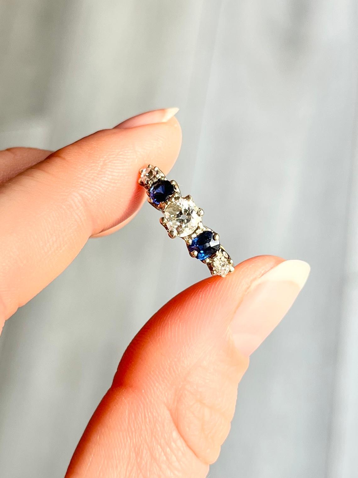 Dieser wunderschöne Ring enthält zwei tiefblaue Saphire von je 25 pt. und drei Diamanten. Der zentrale Diamant misst 50 Pence und die kleineren Diamanten jeweils 7 Pence. Der Ring ist aus 18-karätigem Gold modelliert und die Steine sind in Platin