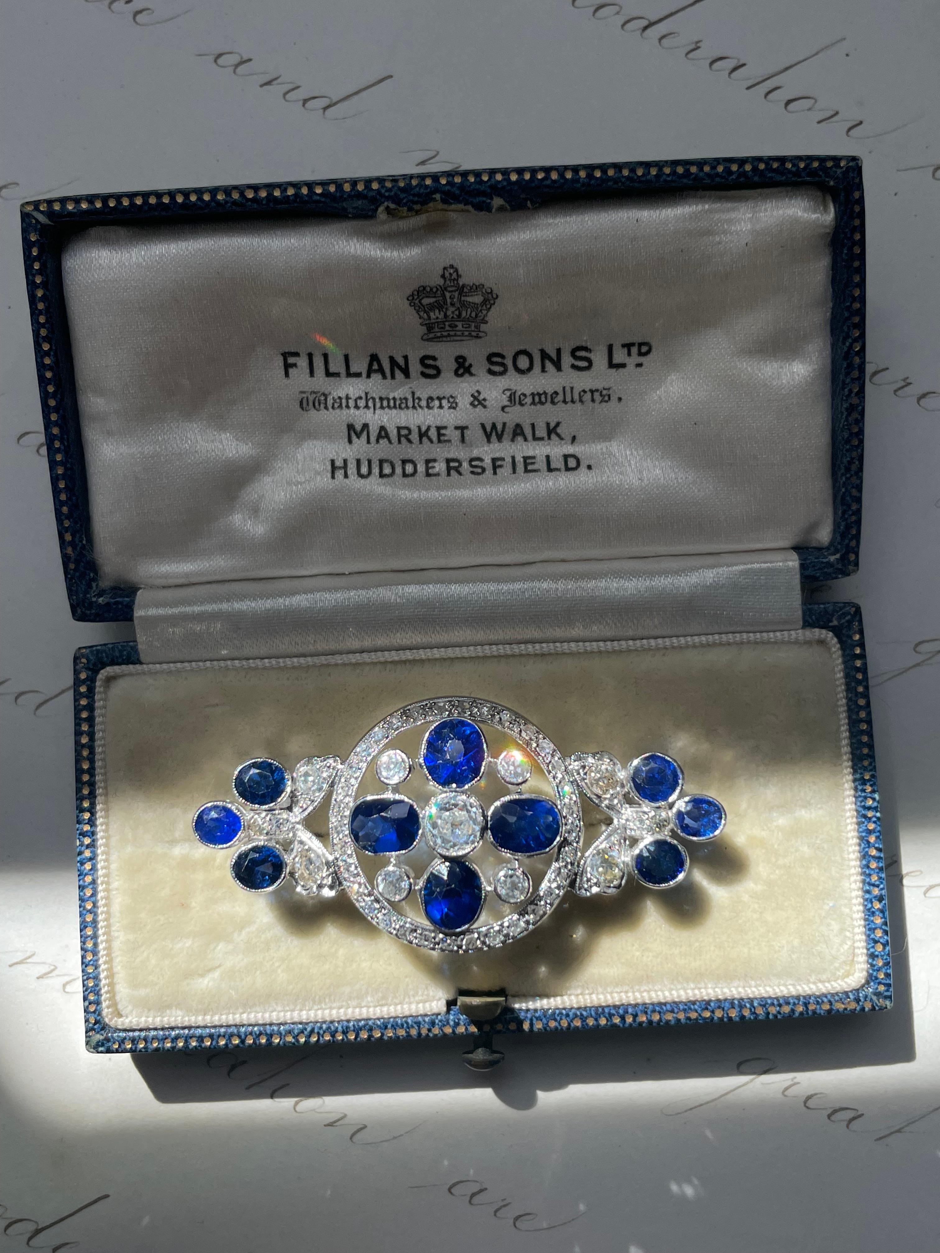 The center of this charming Edwardian / Art Deco brooch is like a tiny flower with petals of natural vivid blue sapphires and shimmering old mine-cut diamonds, floating within a frame lined with glittering single-cut diamonds, finished with sapphire