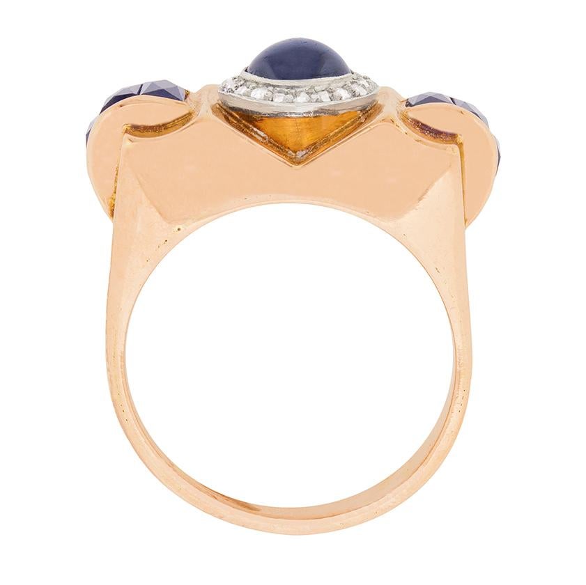 This unique cocktail ring dates back to the Art Deco era, around the 1920s. It is amde in 18 carat rose gold and features a 0.50 carat cabochon cut sapphire in the centre, which is haloed beautifully by diamonds. The diamonds are rose cuts with a