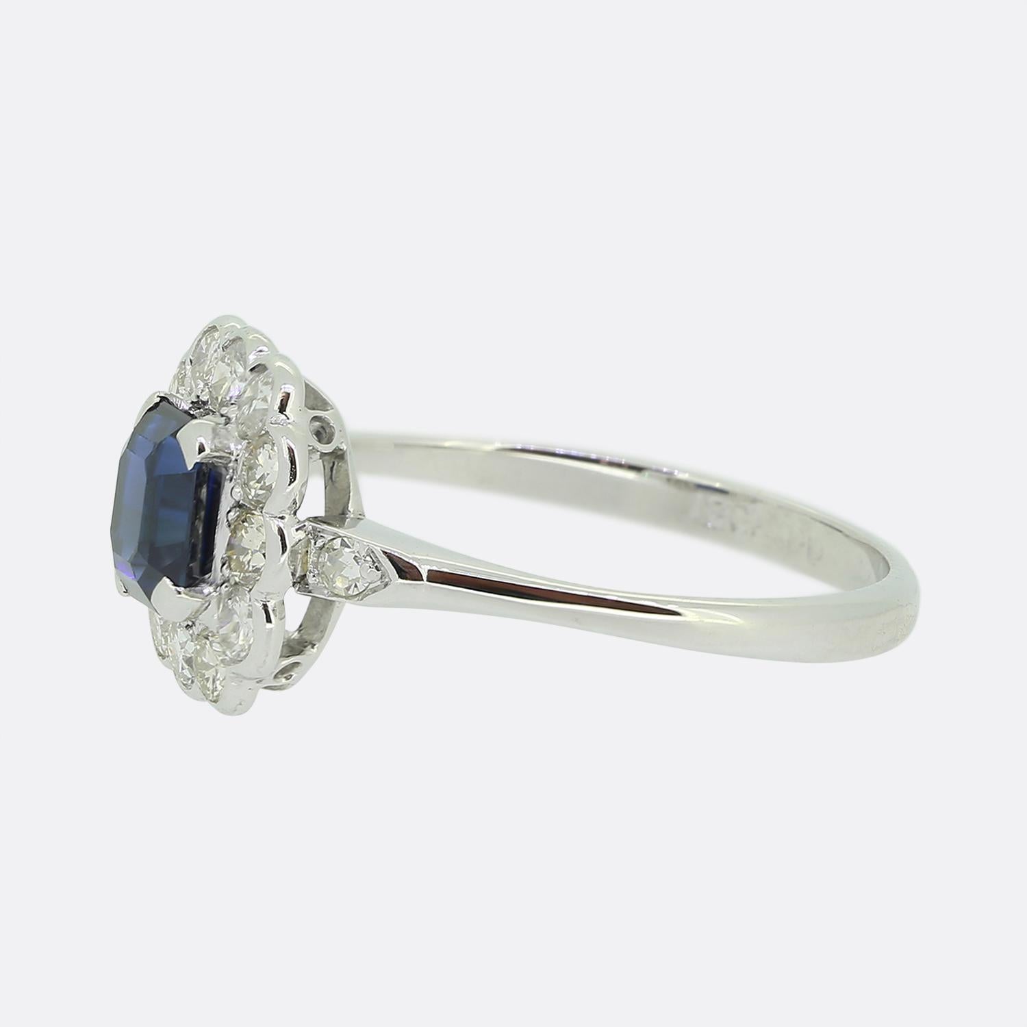 This is a wonderful sapphire and diamond cluster ring dating back to the Art Deco era. The central sapphire is a square step cut and a mid to dark blue hue. The colour of the sapphire is highly complimented by the contrasting bright white sparkle of