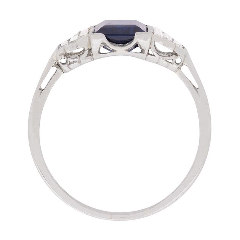 This geometric masterpiece features a 1.40 carat deep blue, natural sapphire as the main attraction. It's a stunning stone, cut into a perfect emerald shape and full of rich colour. It is rub over set and then wonderful supported by diamond baguette