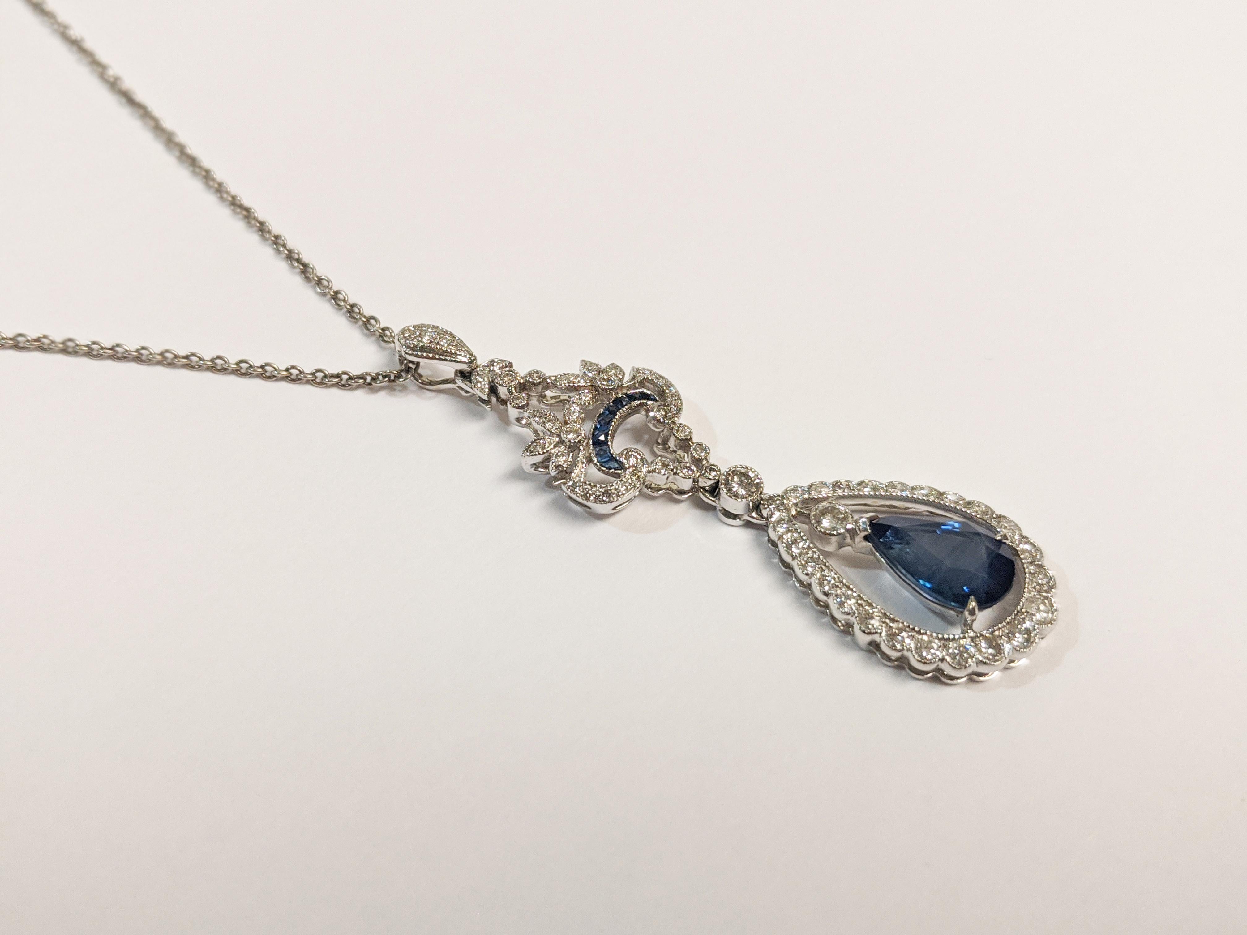 This Art Deco style drop pendant features one pear-shaped blue sapphire of nearly two carats.  Surrounding the center stone are more than 50 round diamonds that sparkle from a scrolling setting. Eight French-cut blue sapphires accentuate the