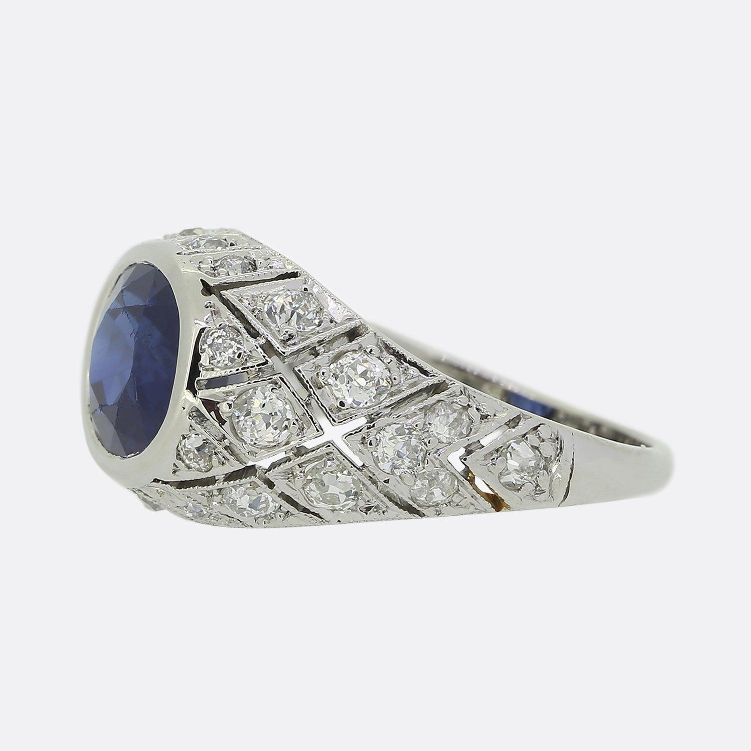 Here we have a magnificent sapphire and diamond ring crafted at a time when the Art Deco style was at the height of design. An oval faceted sapphire possessing a rich indigo colour tone sits at the centre of the face in a rub-over setting. This