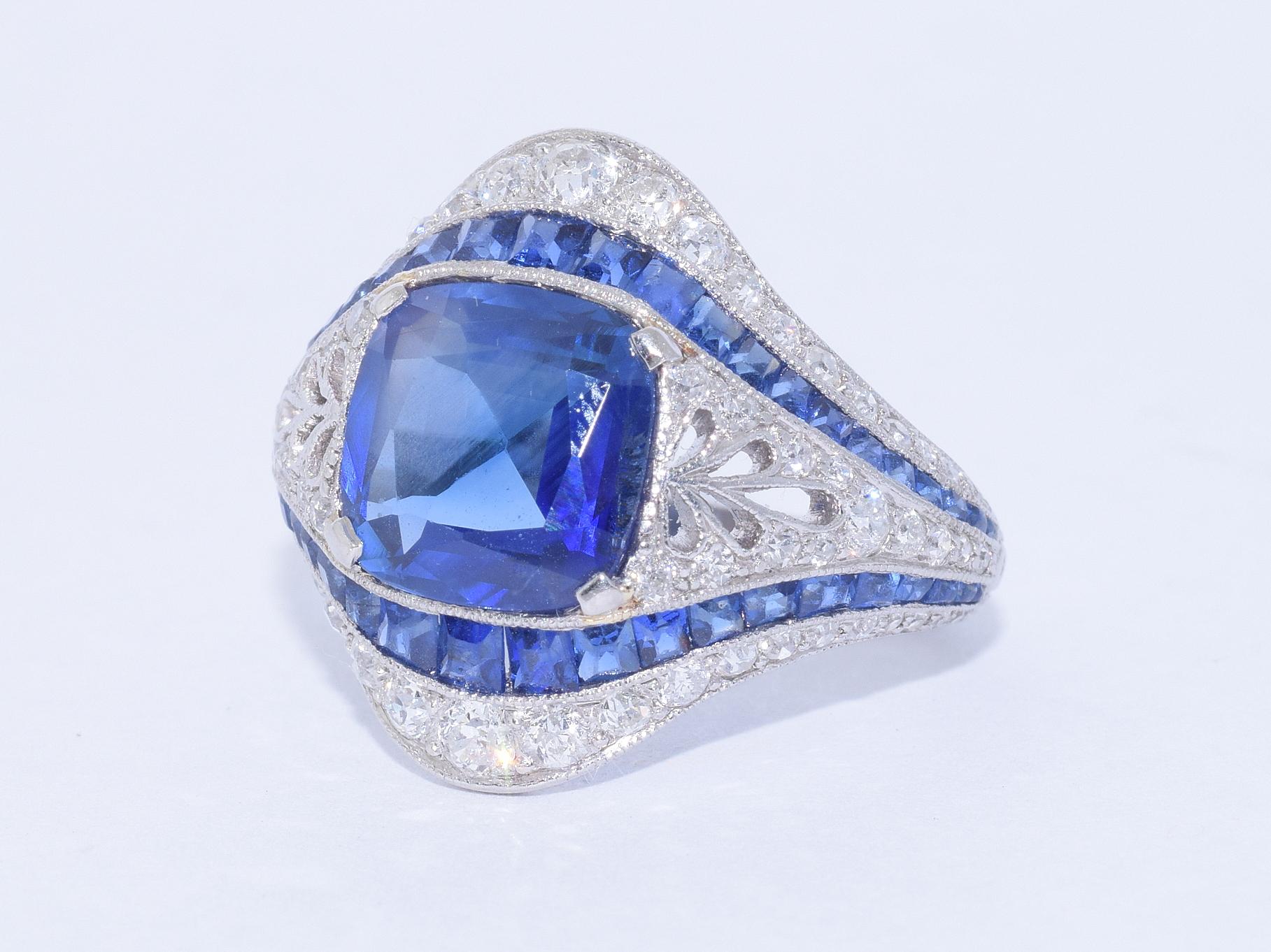 A cushion sapphire weighing 2.80 carats, with gemological report stating there are no indications of heat treatment, is set in a platinum mounting with pierced details accented with a total of approximately 0.80 carat of round diamonds and calibré