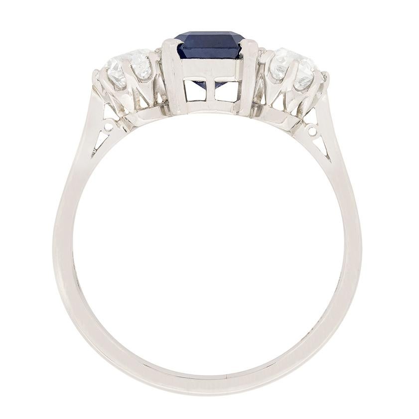 This beautiful art deco piece highlights a wonderful blue sapphire in the centre. It is a natural stone, square emerald cut, held by a four claw corner setting made of platinum. Either side are top quality, old cut diamonds. Each one weighs 0.50