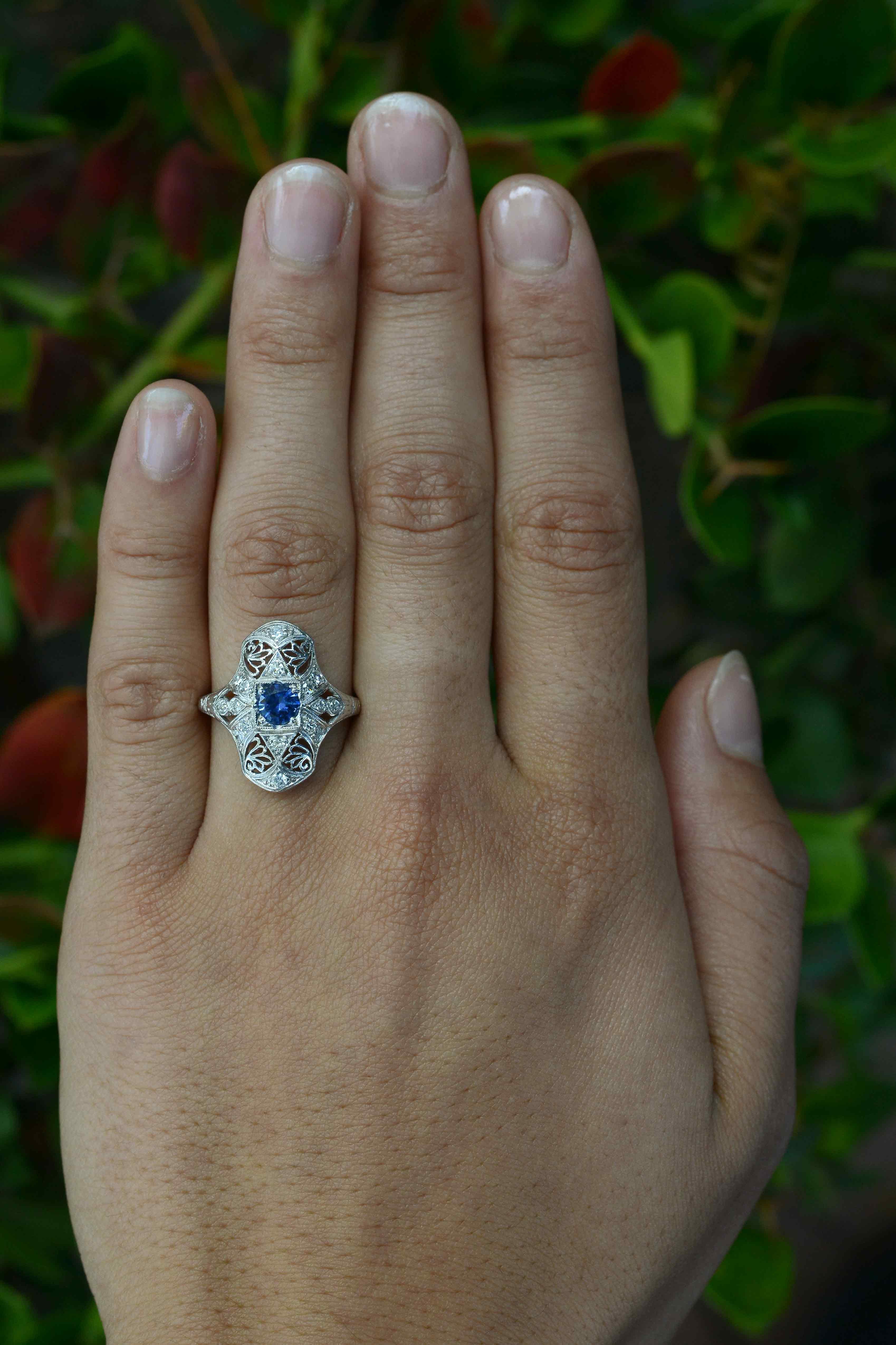 One of the sweetest Art Deco filigree cocktail rings we've ever seen. The delicate platinum floral openwork centered by a captivating natural blue sapphire, shimmering with an intriguing violet blue. Antique Edwardian engagement rings often held