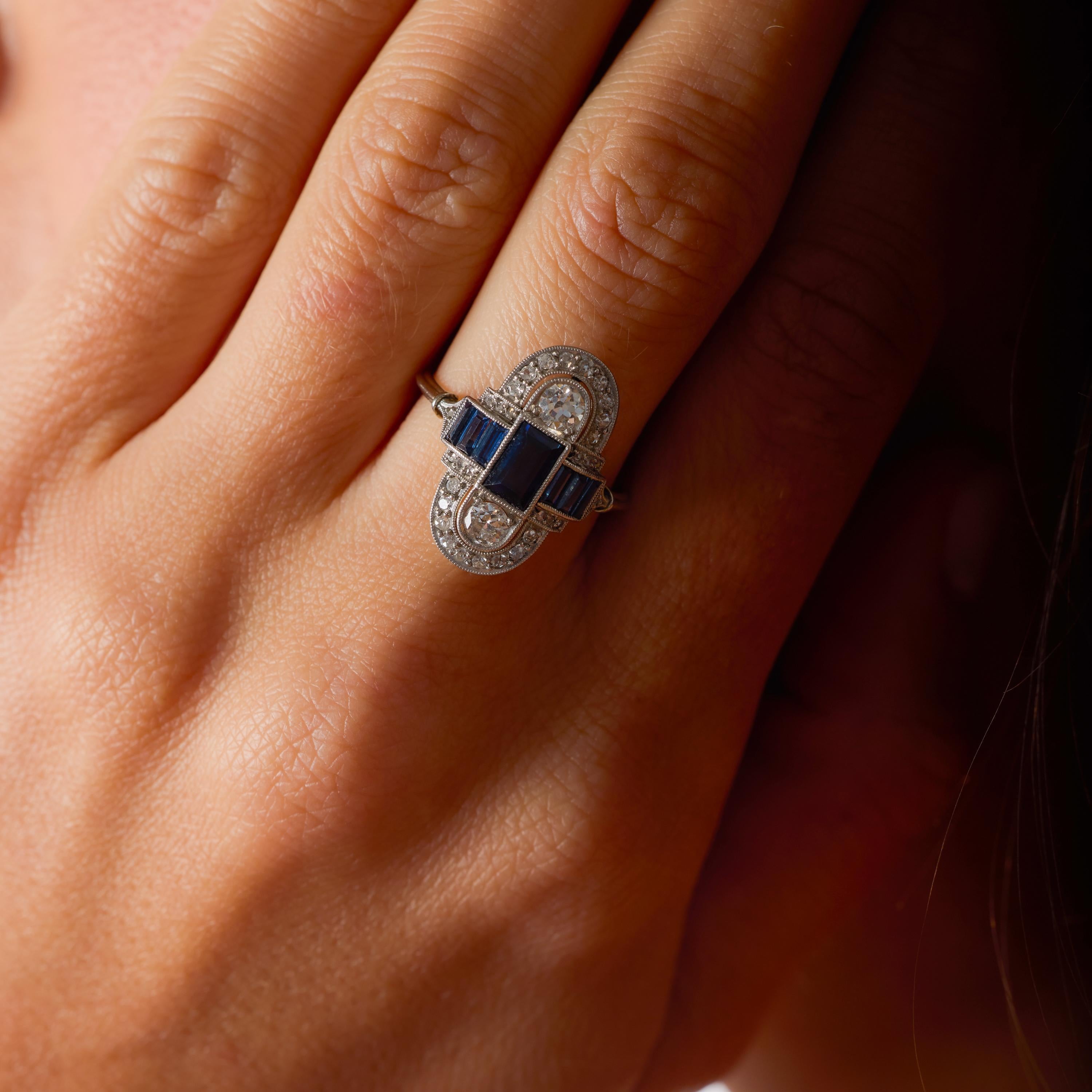 Este impresionante anillo Art Decó captura la audaz geometría y la glamurosa sofisticación que definieron la década de 1930. En su centro, una llamativa disposición de siete zafiros alargados de talla baguette -que en conjunto pesan aproximadamente