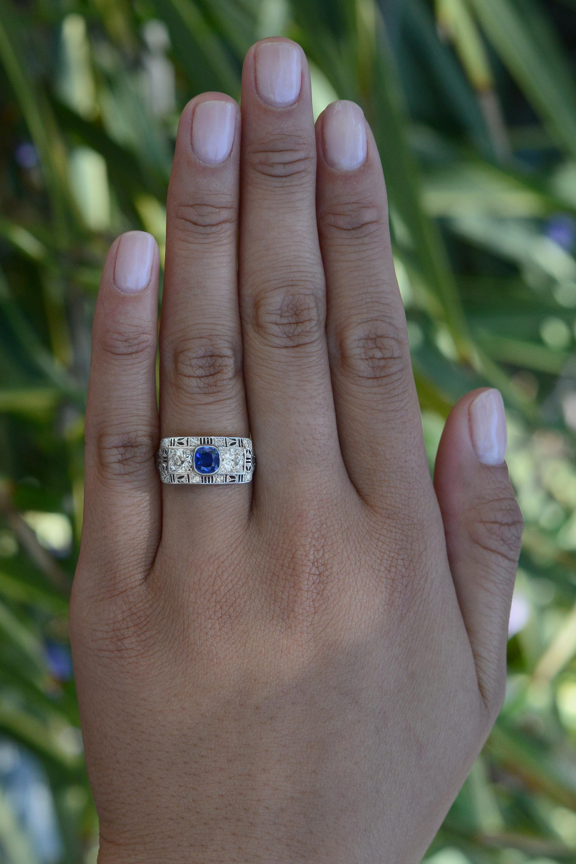 An authentic Art Deco engagement ring, featuring a prominent French design crafted in the great jazz era of the 1920s. The center deep ocean blue sapphire is flanked by 2 old European circular diamonds presenting excellent clarity and life. Boasting