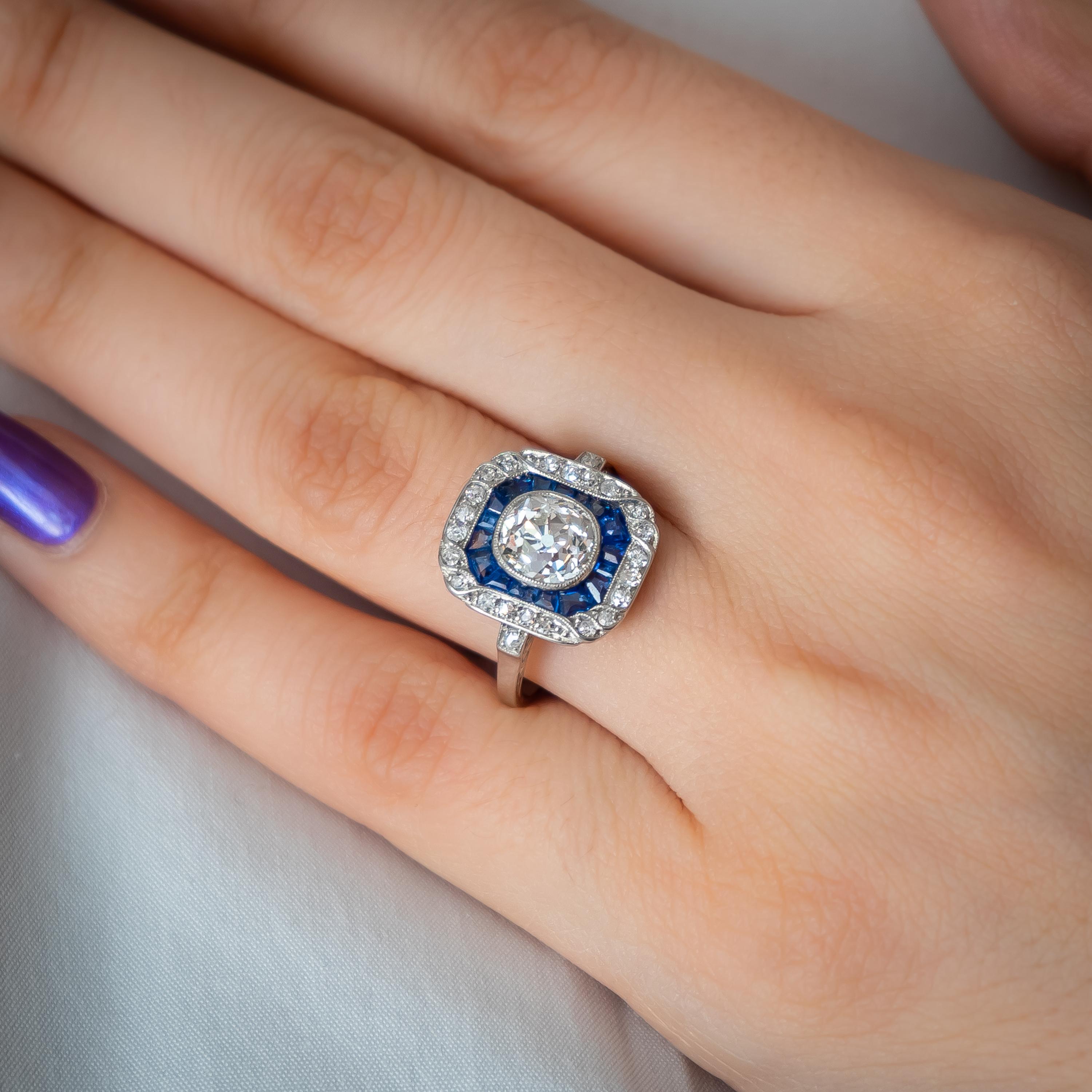 An Art Deco sapphire and diamond ring, with a central old cut diamond, weighing an estimated 1.30ct, in our opinion the colour is I and our opinion of the clarity is VS, in a millegrain edged rub over setting, surrounded by calibré-cut sapphires,
