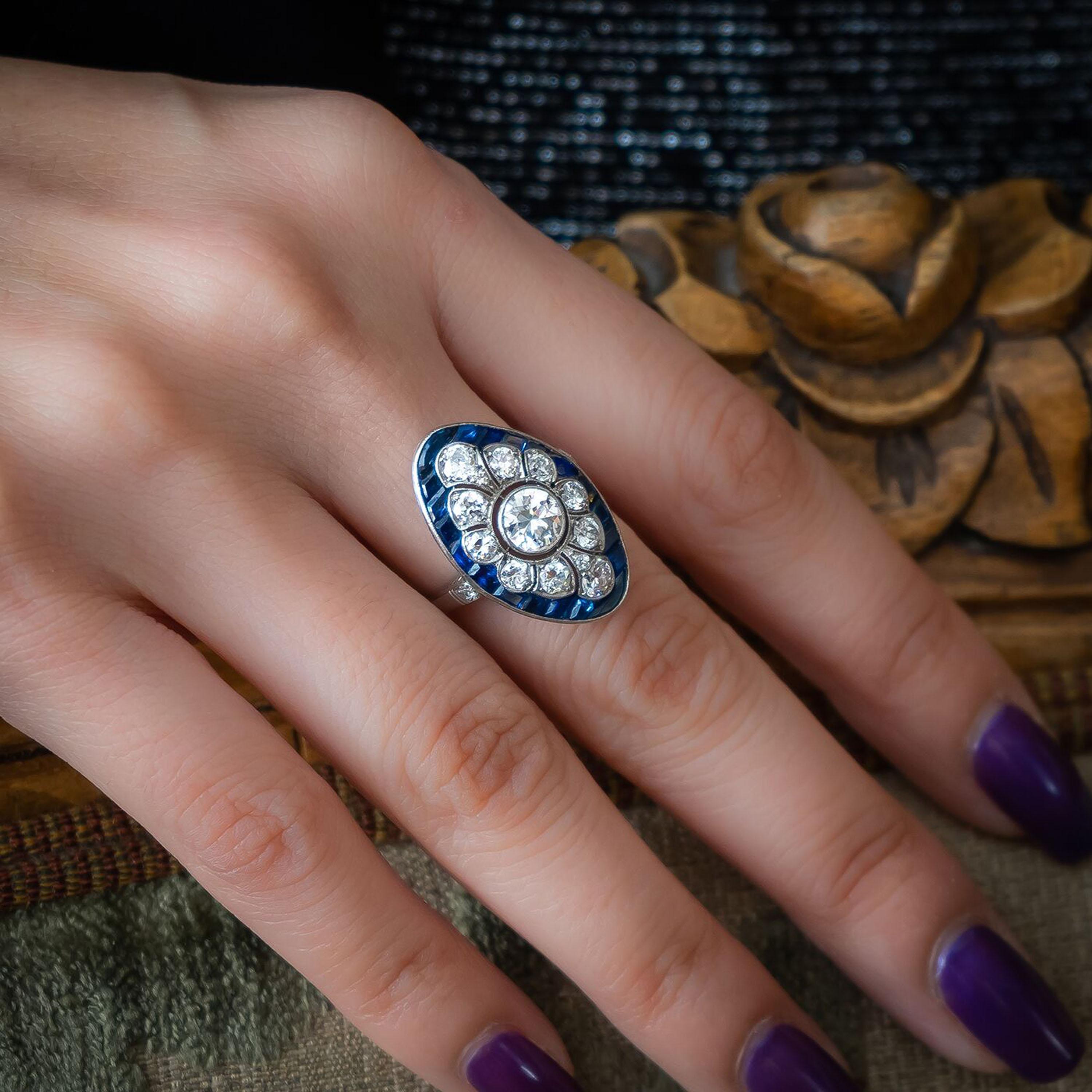 An Art Deco sapphire and diamond oval plaque ring, with an Edwardian-cut diamond, in the centre of a decorative openwork cluster of round brilliant and Edwardian-cut diamonds, in millegrain edged rub over and grain settings, superimposed on a