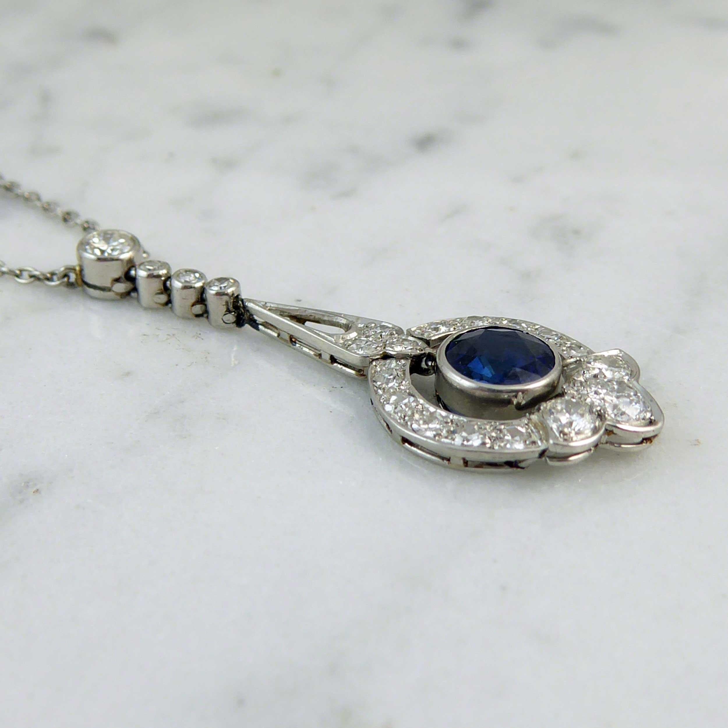Art Deco necklace set with sapphire and diamonds comprising a round mixed cut blue sapphire articulating to the centre of a rectangular cross section wire hoop.  The hoop has a fleur-de-lys style base set with three brilliant cut diamonds whilst the