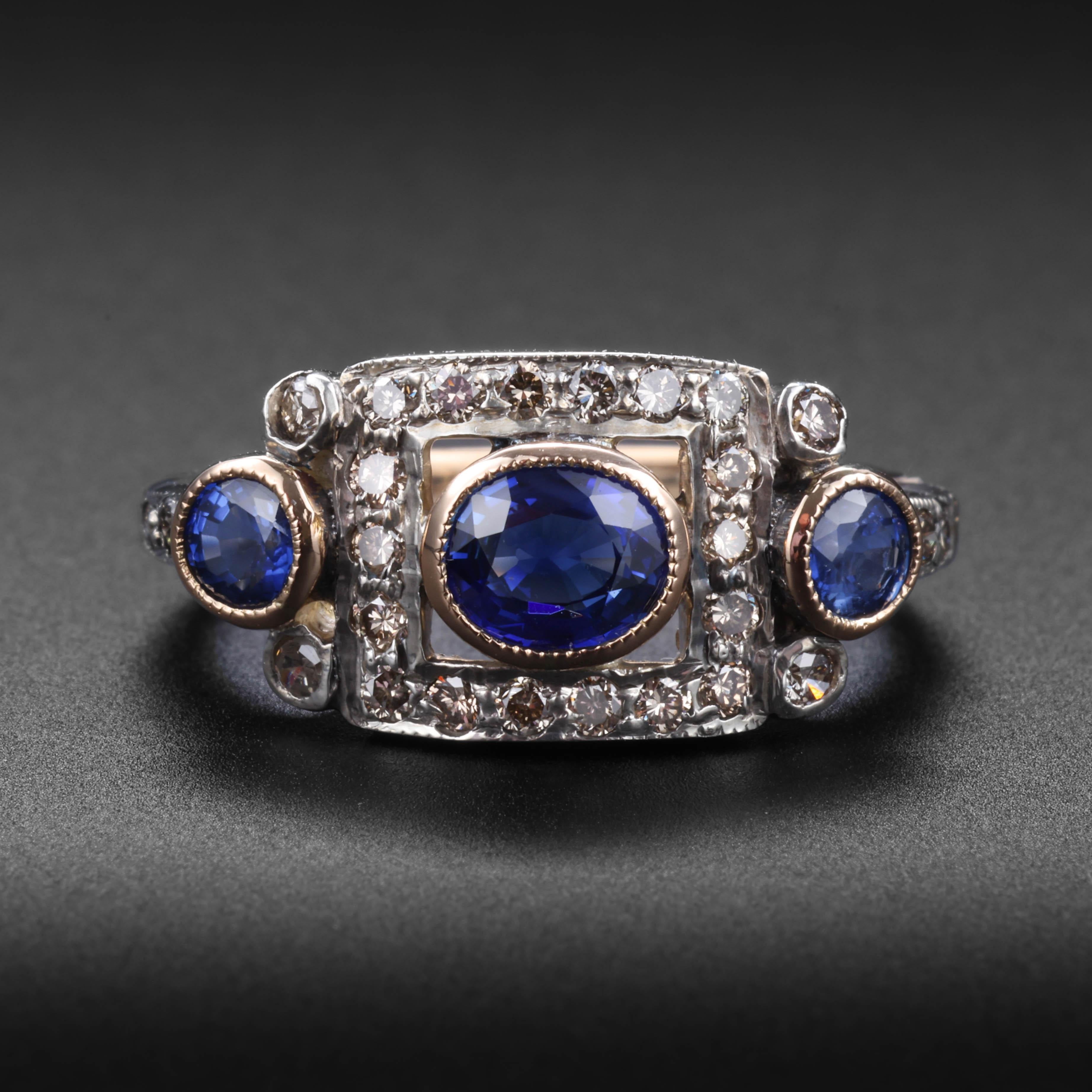 This Art Deco 18K gold and platinum ring features a trio of bright blue bezel-set sapphires complimented by 22 Old European-cut diamonds. The old diamonds are a pleasing blend of warmer tones. 

Rising just 4.3mm from the surface of the finger, this