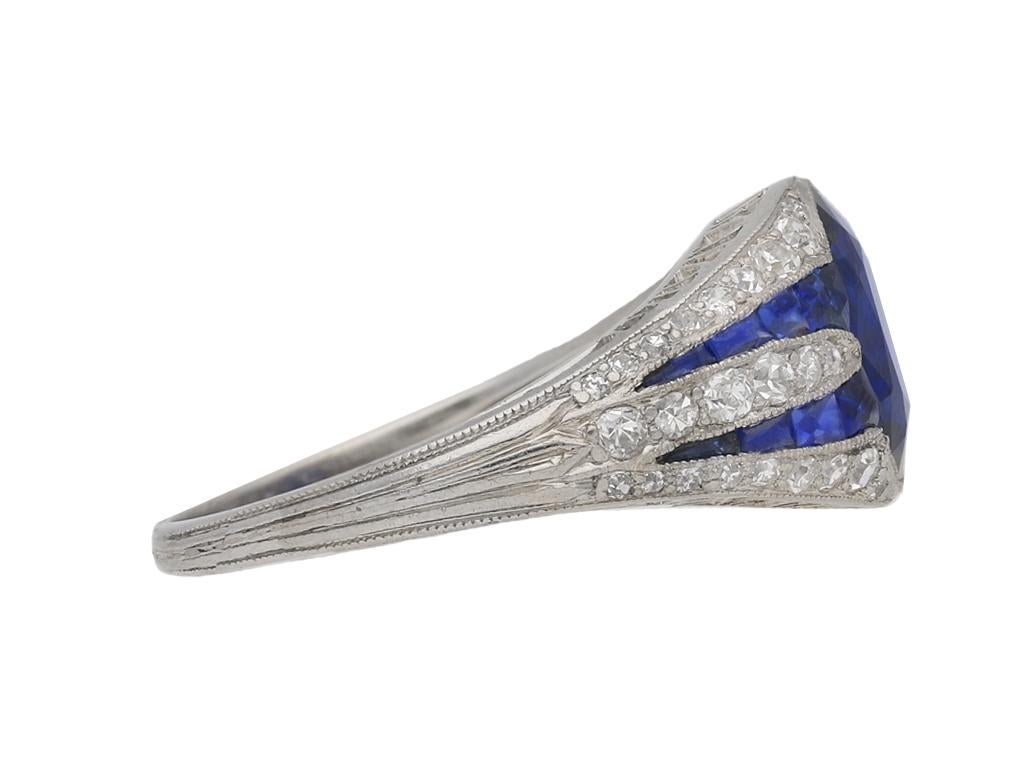 Art Deco sapphire and diamond ring. Set to centre with an oval old cut natural unenhanced sapphire in an open back rubover millegrain setting with an approximate weight of 2.00 carats, flanked by sixteen tapered channel set calibre cut sapphires in