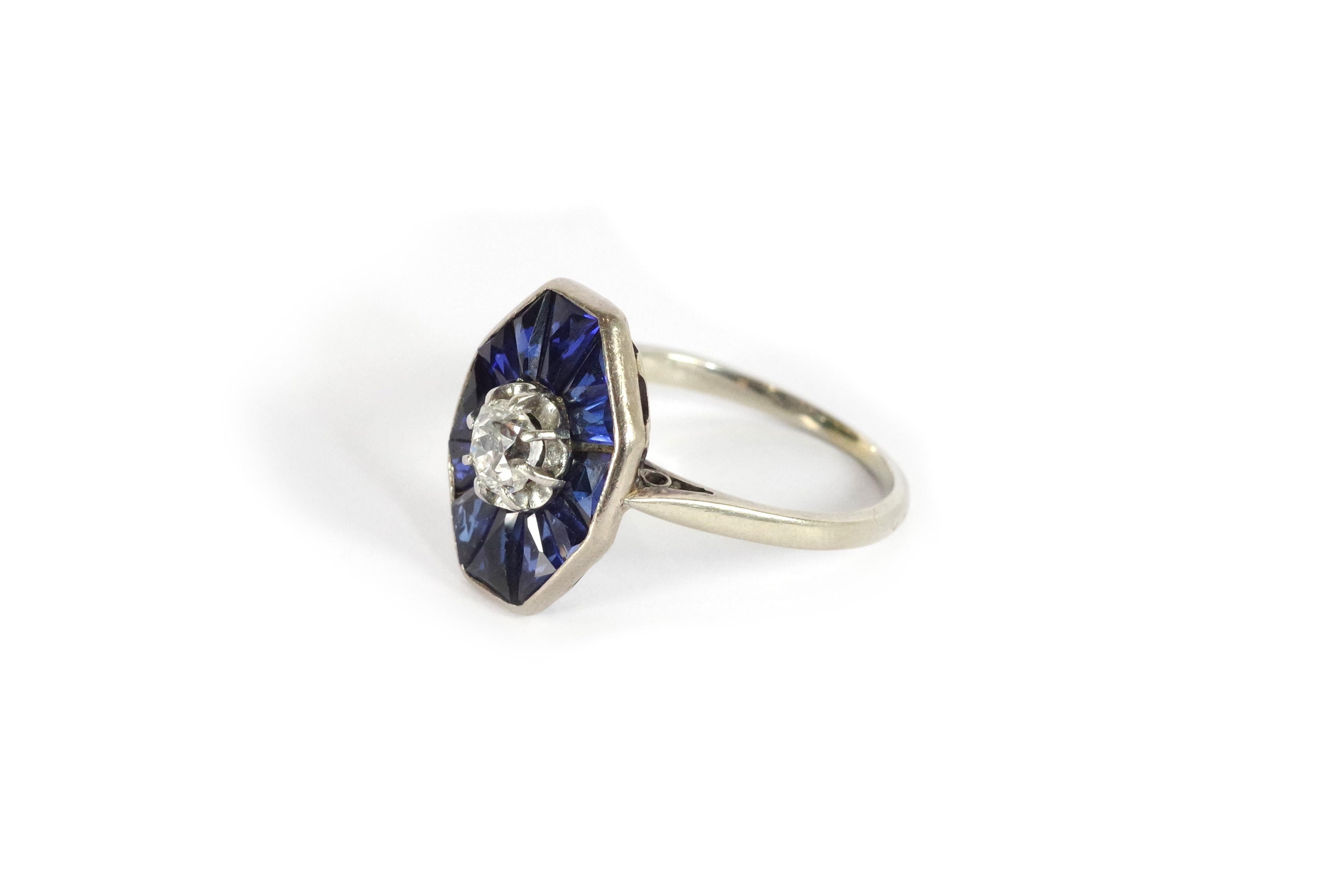 Art Deco sapphire platinum ring in 18 karat white gold and platinum. Octagonal Art Deco ring with an old mine cut diamond, approx. 0.20 carat. The diamond is surrounded by triangular faceted synthetic sapphires. The ring features the geometric