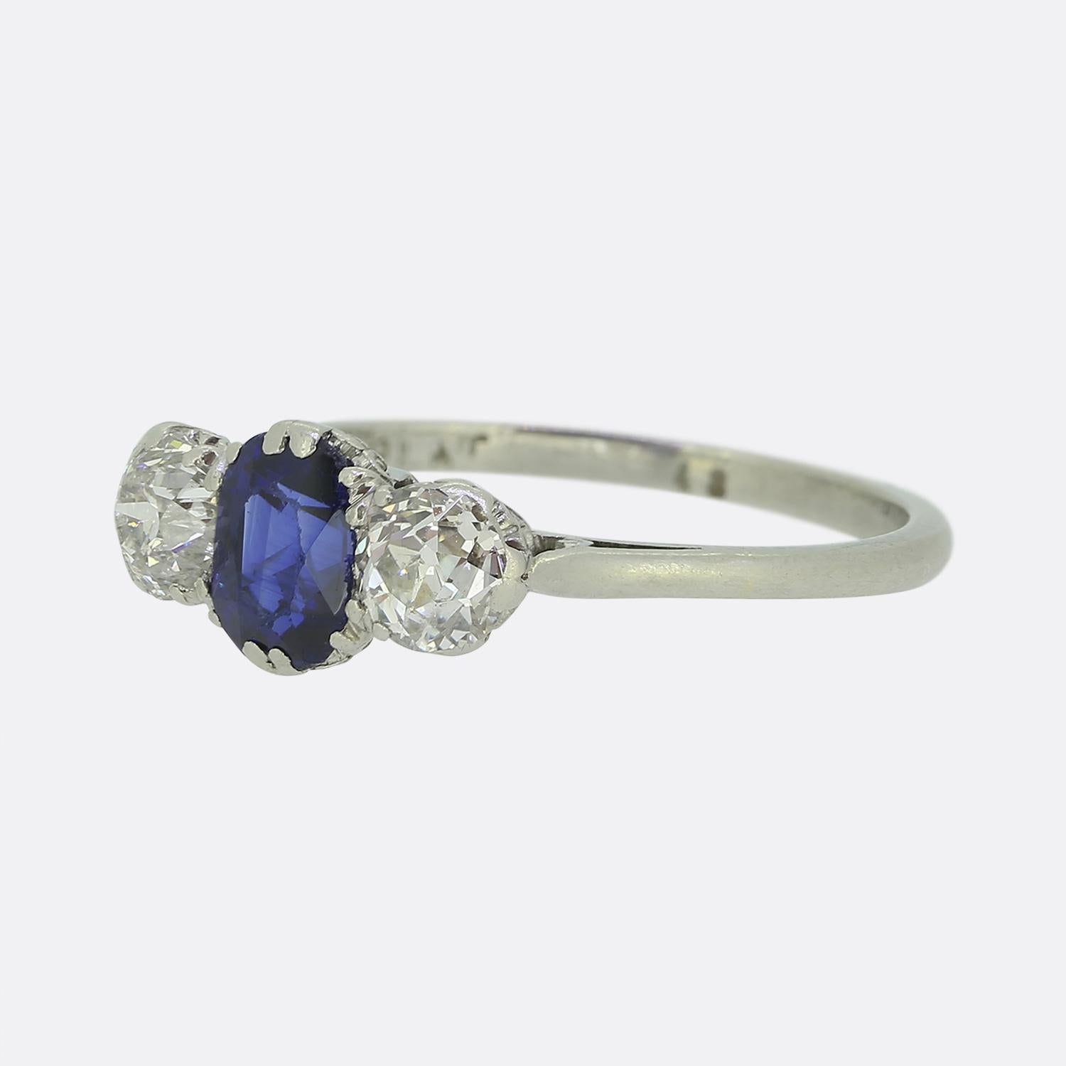 Nous avons ici une fabuleuse bague Art déco à trois pierres. Au centre du visage se trouve un saphir bleu captivant, d'une riche couleur bleu moyen à bleu foncé. La pierre principale est ensuite flanquée de part et d'autre d'un diamant rond à