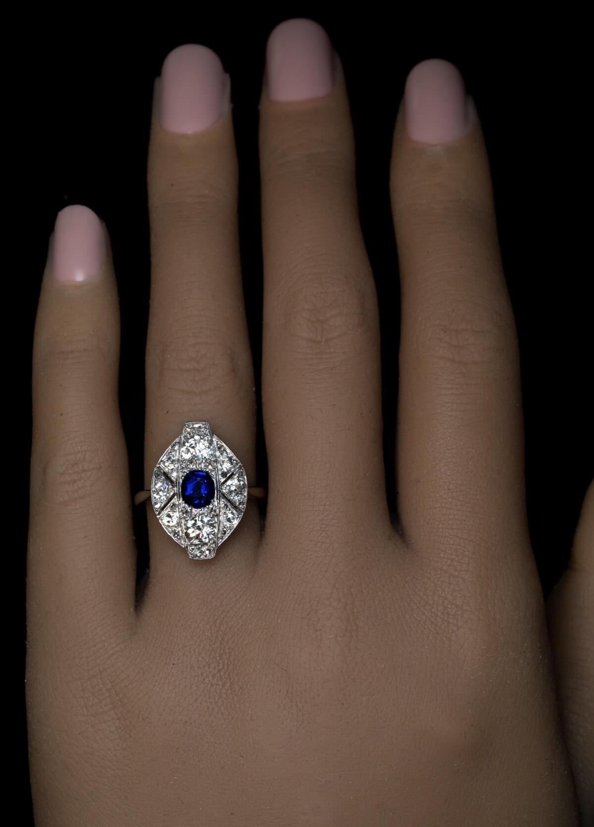 Circa 1925  This distinctly Art Deco ring is crafted in white 18K gold. It is centered with an oval royal blue sapphire (approximately 0.67 ct) framed by bright white old European cut diamonds (G-H color, VS2 average clarity), accented by small rose