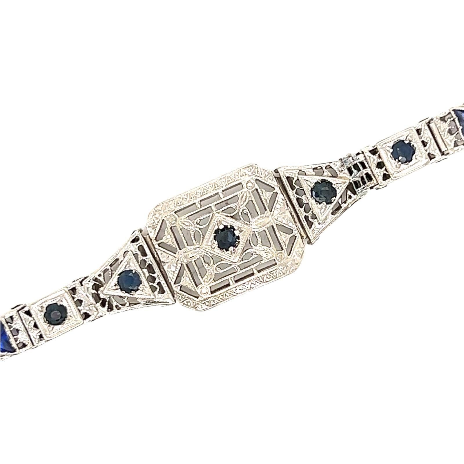 Original Art Deco filigree bracelet crafted in 14 karat white gold. The bracelet features synthetic sapphire accents which were indicative of the time. The bracelet measures 7.0 inches in length, .50 inches in width, and features box clasp with
