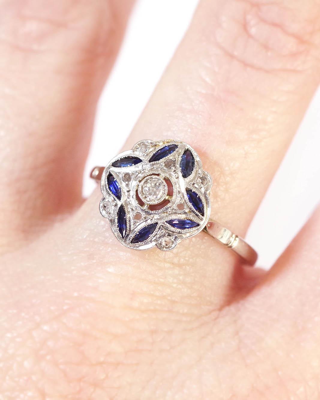 Art Deco sapphire platinum ring in 18 karat white gold and platinum. Antique ring with four-lobed bezel, set with a 0.08-carat old-cut diamond in the center. The top is decorated with eight navette-cut (synthetic) sapphires and eight rose-cut