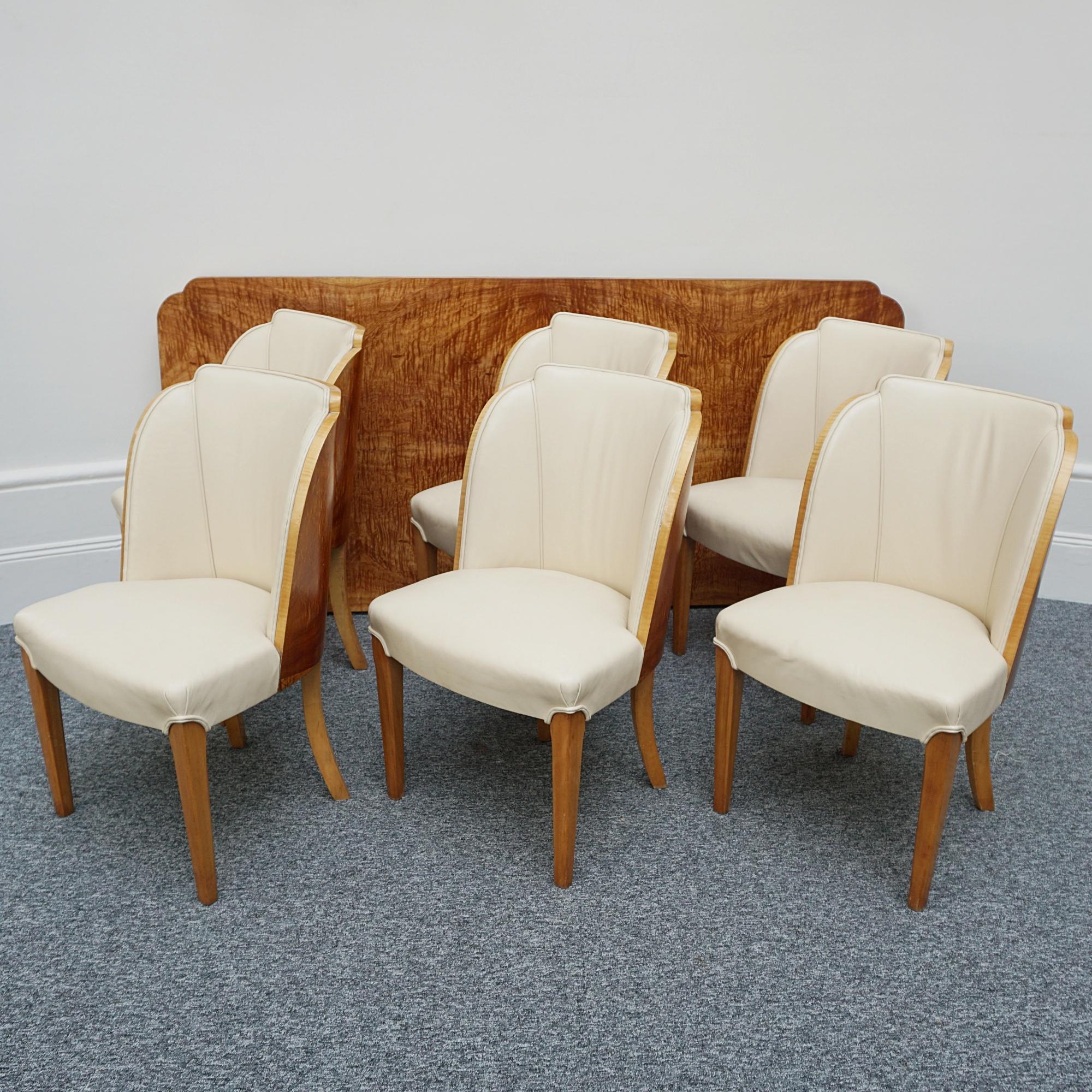 An Art Deco six seater dining suite by Harry & Lou Epstein. Satinwood veneered six - eight seater table top set over satinwood veneered pedestal base. Six matching cloud backed armchairs with satinwood veneer. Cream leather upholstery. 

Dimensions: