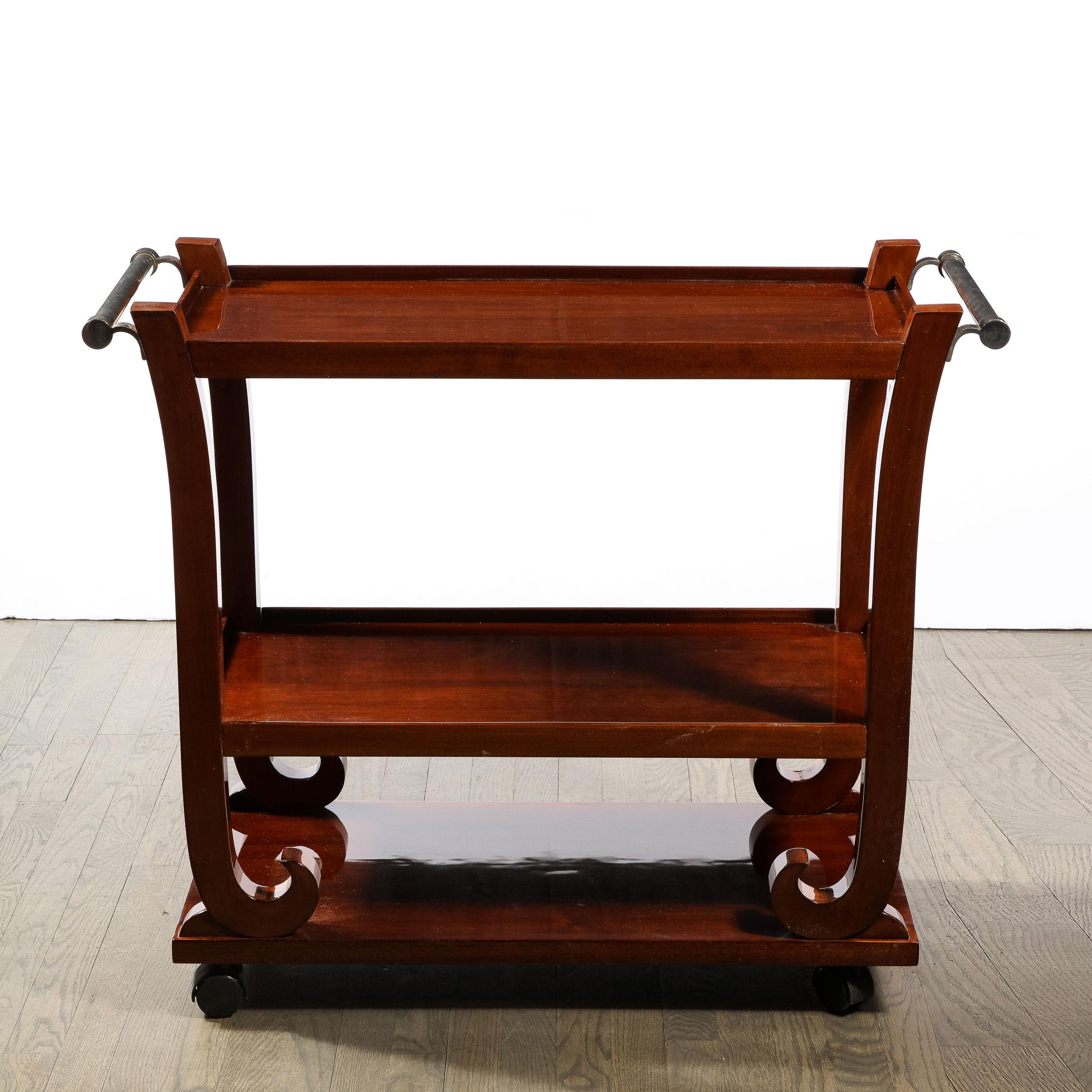 This elegant three tier bar cart was realized in France circa 1940. Sitting on castors- allowing for effortless transport- the piece is composed of solid bookmatched walnut- consisting of a base, a top, and a central tier connected by a curvilinear