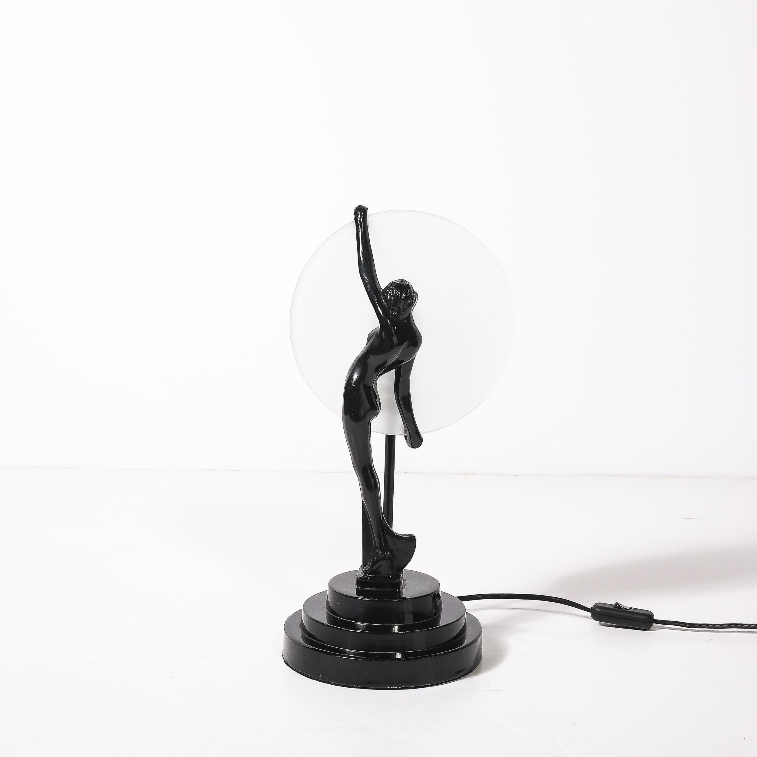 This captivating Art Deco table lamp captures the glamour of the roaring twenties with its sculptural design inspired by the iconic flapper aesthetic. The lamp features a detailed sculptural base finished in lustrous black enamel, showcasing a