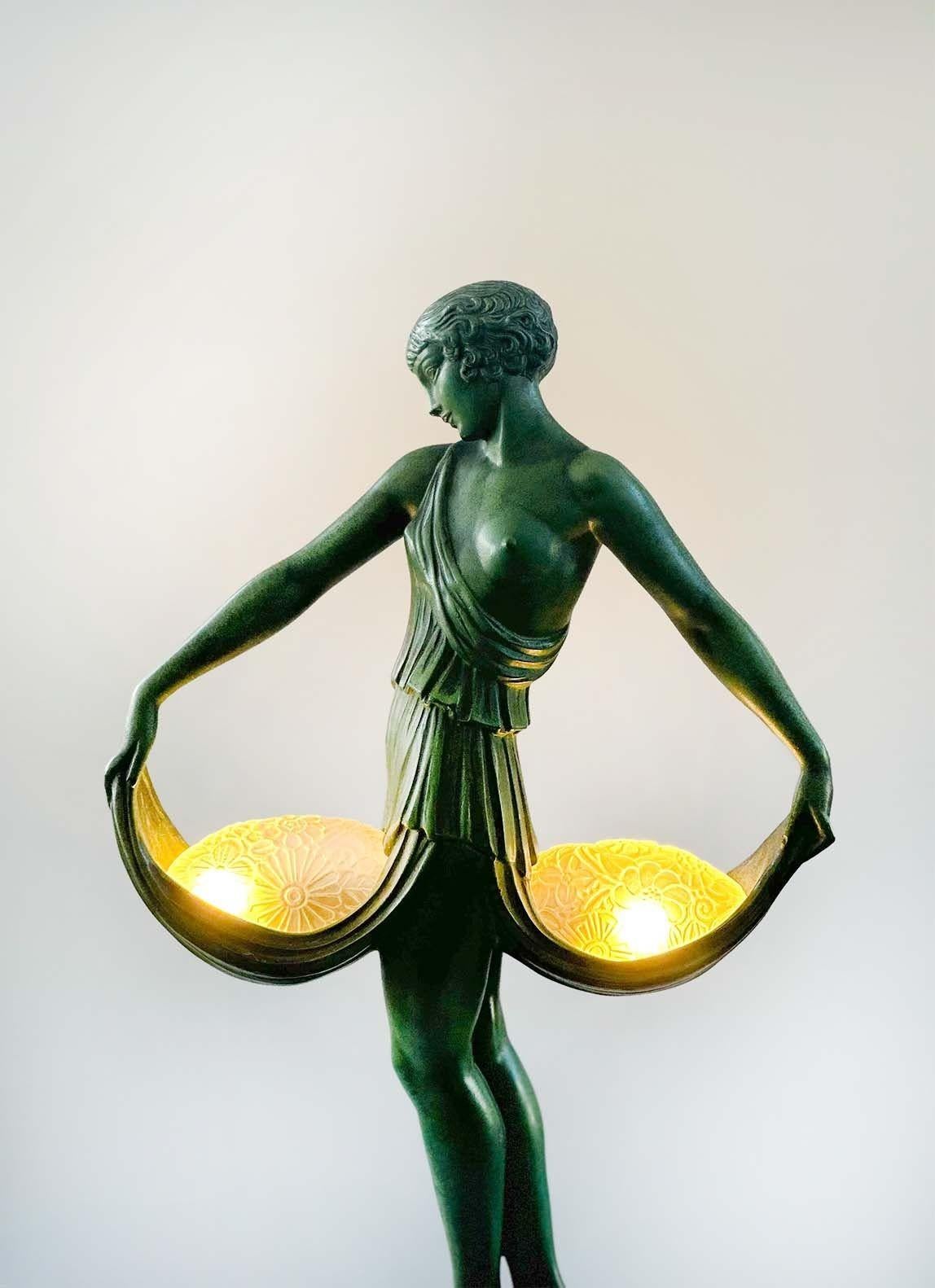 Beautiful Art Deco verdigris patinated metal sculptural table lamp by Pierre Le Faguays, France c. 1930. It depicts a female dancer standing on a marble base holding her attire gracefully which hold two molded glass shades with floral details.