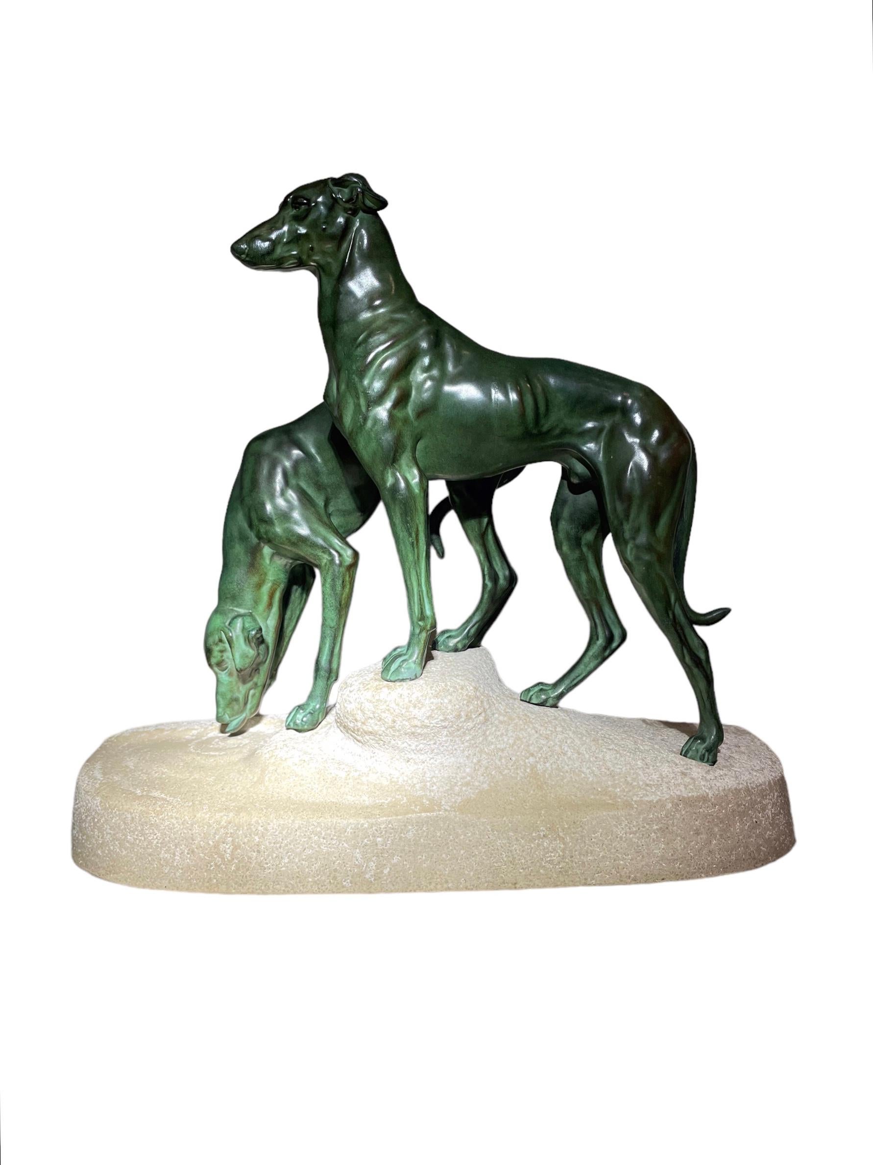 Cette sculpture d'époque Art déco de deux chiens courants en métal, dont l'un est debout tandis que l'autre boit dans un bassin d'eau, est posée sur un socle en grès naturaliste, conçu et créé par le célèbre sculpteur animalier Jules-Edmond Masson