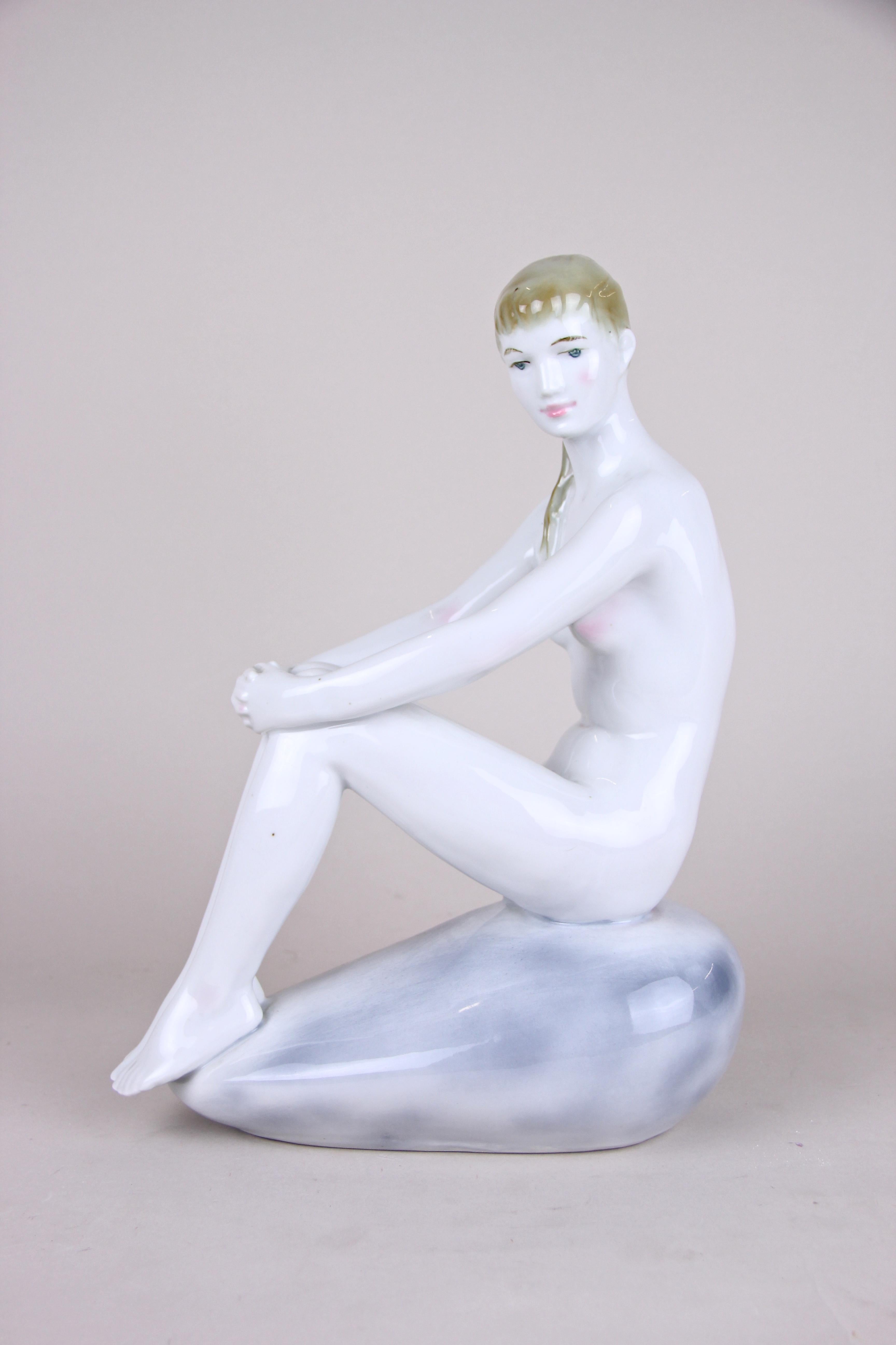 Lovely Art Deco porcelain sculpture by the renown manufactory of Zsolnay Pecs from Hungary around 1930. This fine polychromed sculpture displays a young nude lady sitting on a small rock and looking dreamily into the distance. It is in absolute