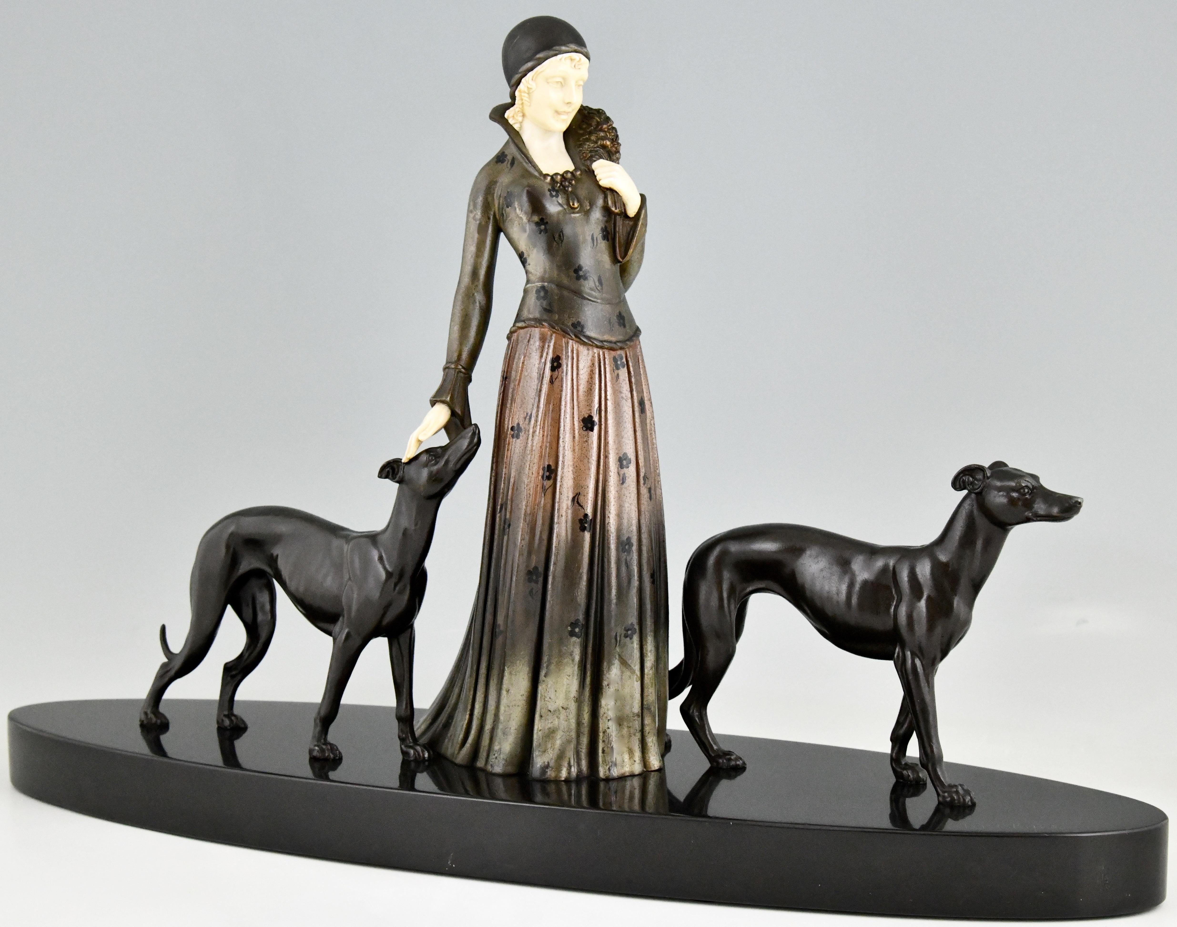 Art Deco sculpture lady with greyhound dogs by Demetre Chiparus on an oval Belgian black marble base. The statue is executed in patinated metal, face and hands of the woman are in ivorine. The dress has very fine details.
This model is illustrated