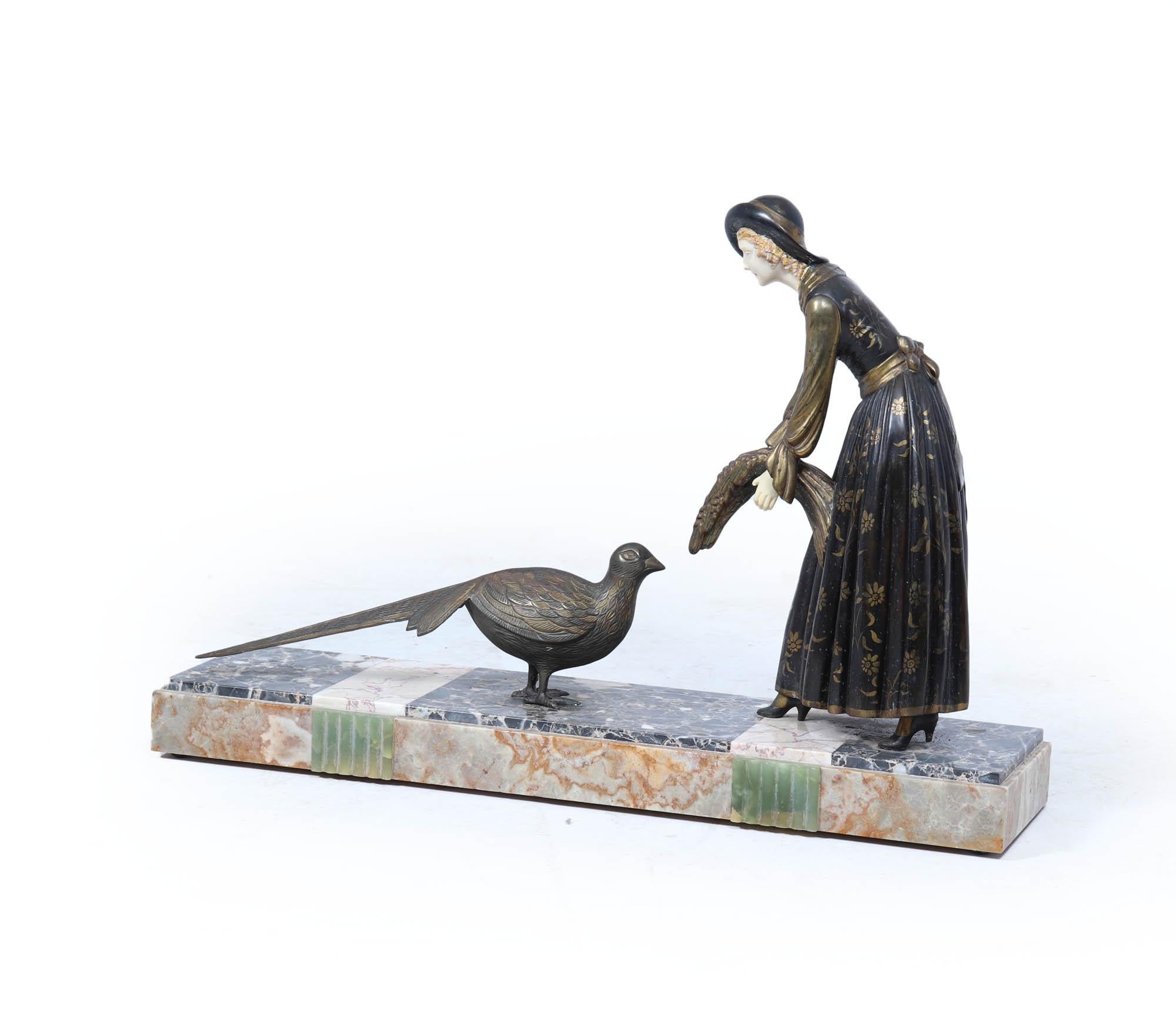 A striking 1930s Art Deco sculpture depicting a woman in a flowing gilt-patterned dress, gently feeding a pheasant. Finely cast in patinated spelter with gilded highlights and mounted on a veined marble base, this decorative piece captures the