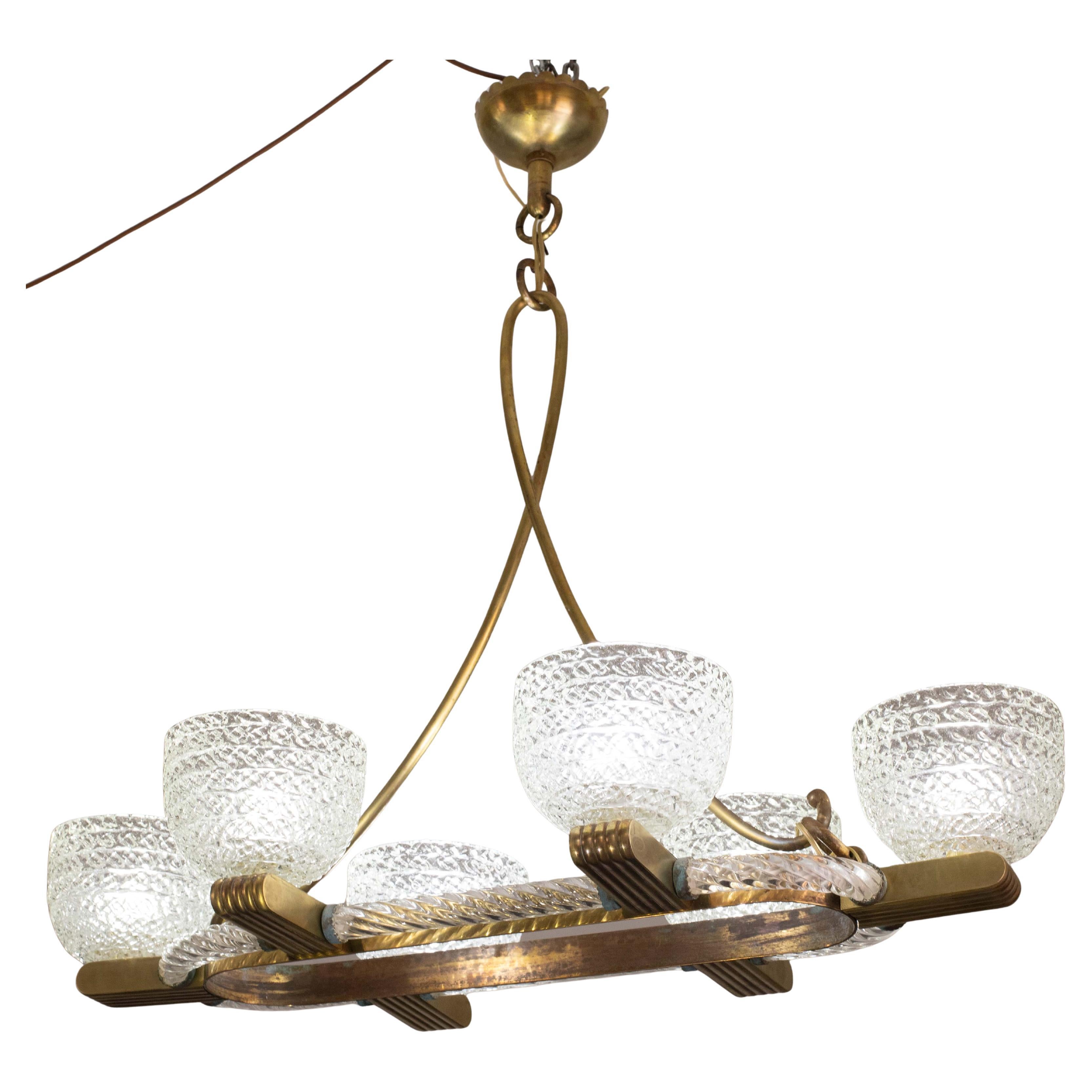 Lampadario ovale a sei luci di Murano attribuito alla vetreria Seguso della metà del secolo scorso, con un anello interno in ottone e un vetro soffiato a spirale all'esterno, da cui si dipartono sei bracci scanalati in ottone che terminano in coppe
