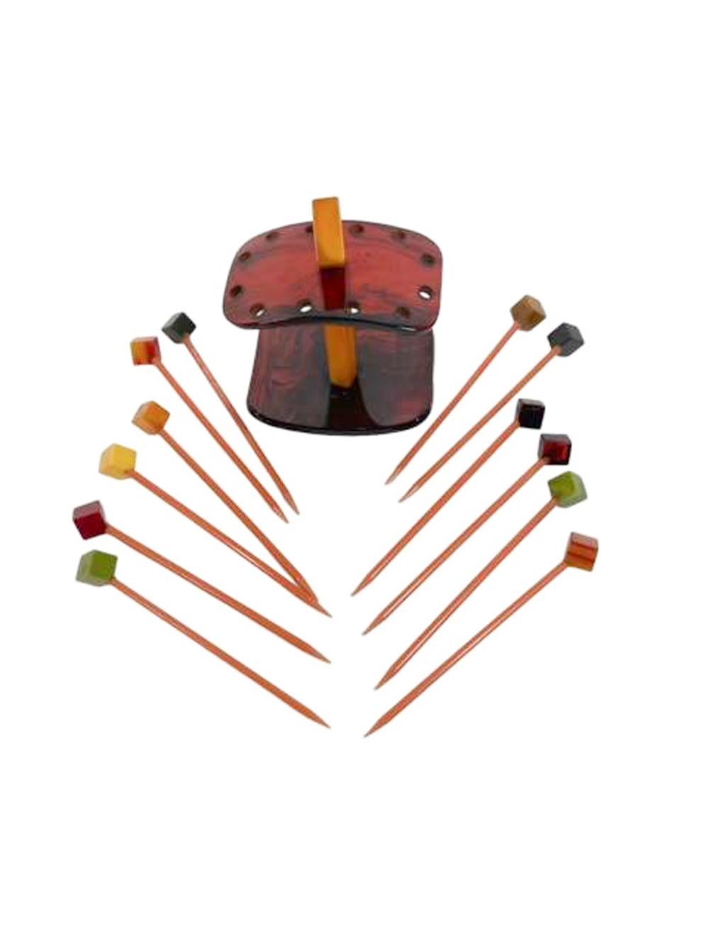 Set of 12 cocktail picks with multicolored Bakelite cube tops mounted angularly  on pointed Bakelite rods in a stand of butterscotch and tortoiseshell Bakelite.