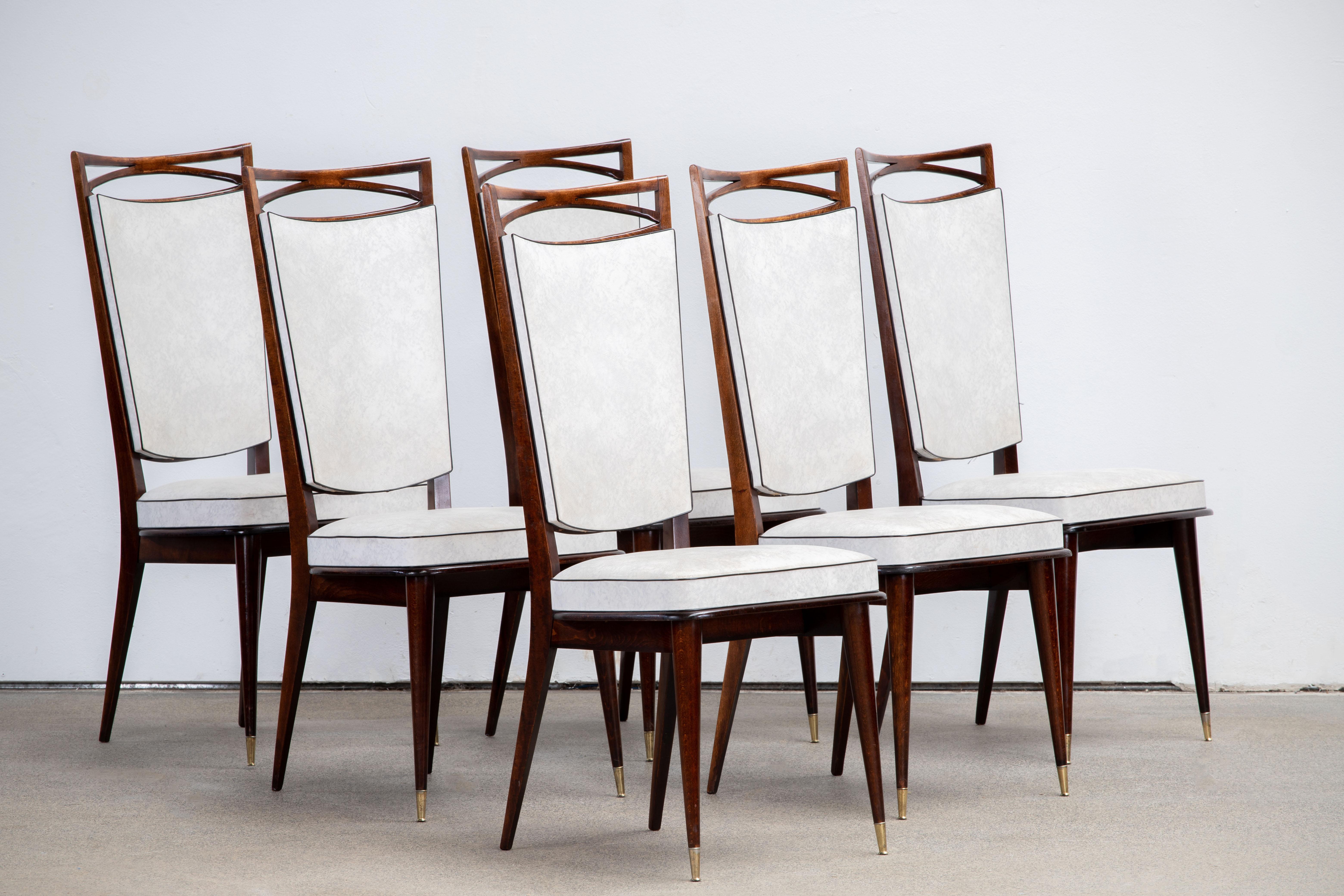Set of six upholstered high back chairs covered in white vynil, exhibiting traditional French design elements in a deep oak finish.

In the style of René Prou, Albert-Lucien Guenot, Pomone, André Arbus, Baptistin Spade, Charles Dudouyt, Herman