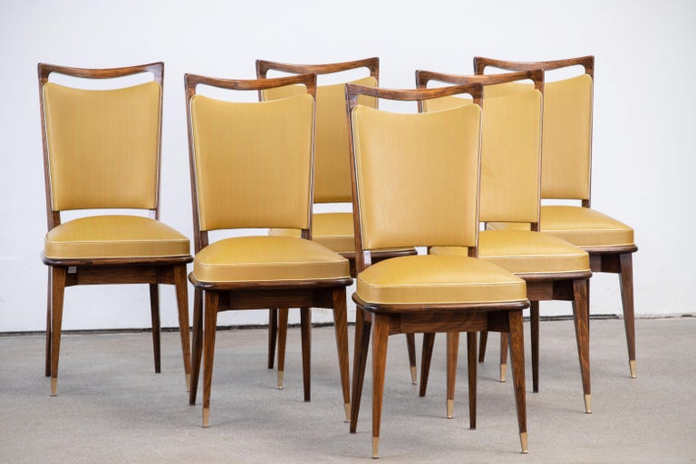 Set of six upholstered high back chairs covered in yellow vynil, exhibiting traditional French design elements in a deep oak finish.

In the style of René Prou, Albert-Lucien Guenot, Pomone, André Arbus, Baptistin Spade, Charles Dudouyt, Herman