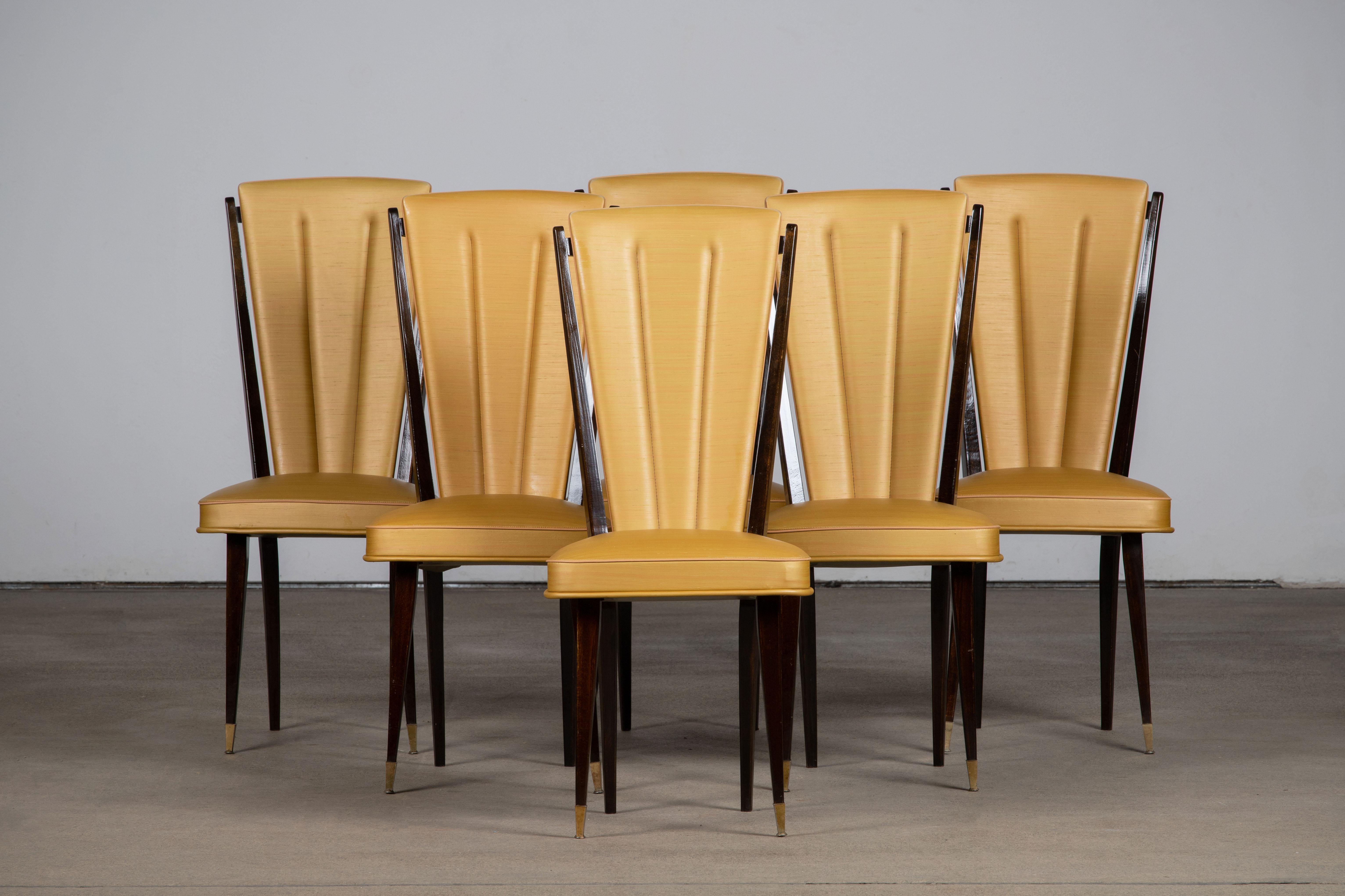 Set of six upholstered high back chairs covered in yellow vynil, exhibiting traditional French design elements in a deep oak finish.

In the style of René Prou, Albert-Lucien Guenot, Pomone, André Arbus, Baptistin Spade, Charles Dudouyt, Herman