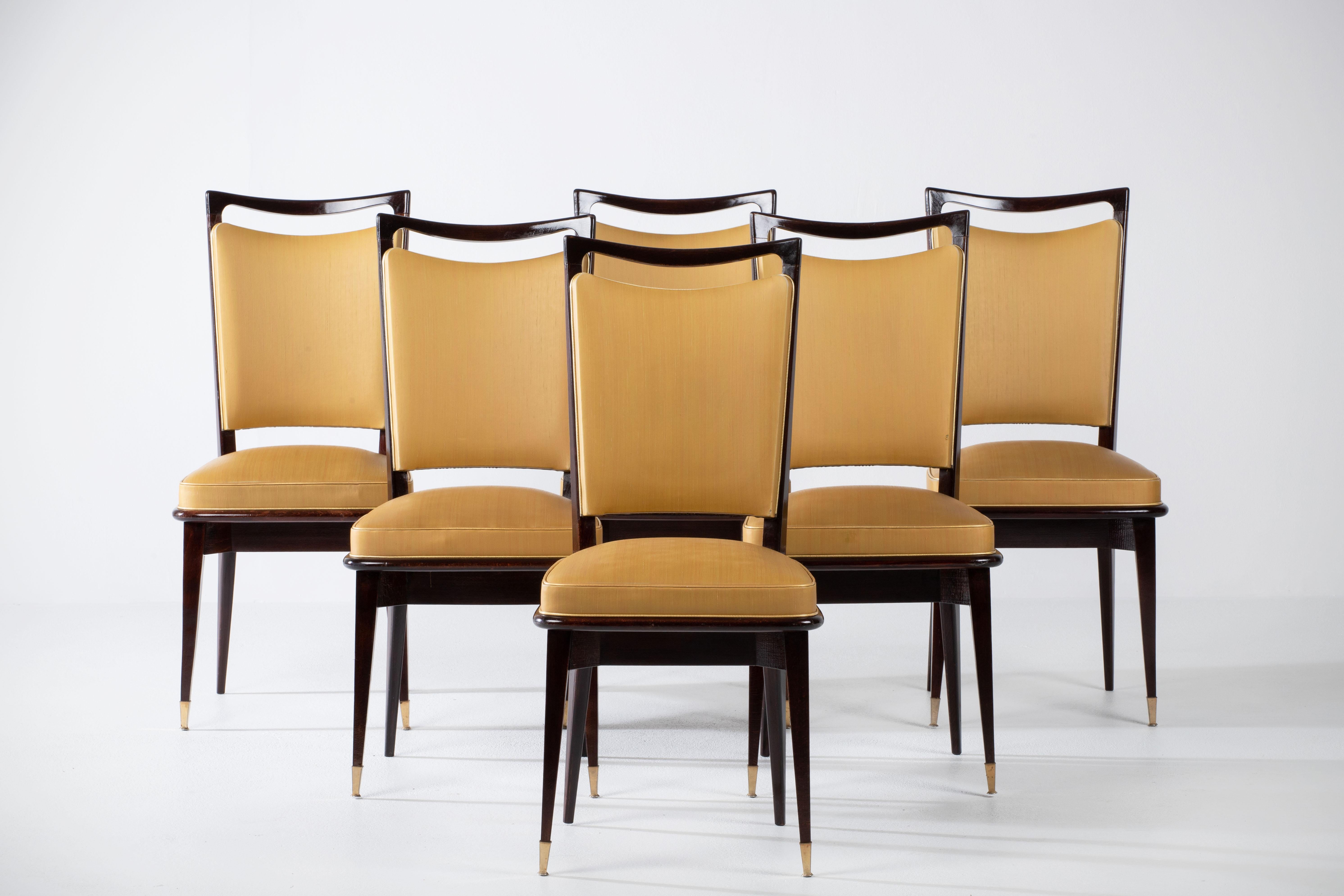 Set of six upholstered high back chairs covered in yellow vynil, exhibiting traditional French design elements in a deep oak finish.

In the style of René Prou, Albert-Lucien Guenot, Pomone, André Arbus, Baptistin Spade, Charles Dudouyt, Herman